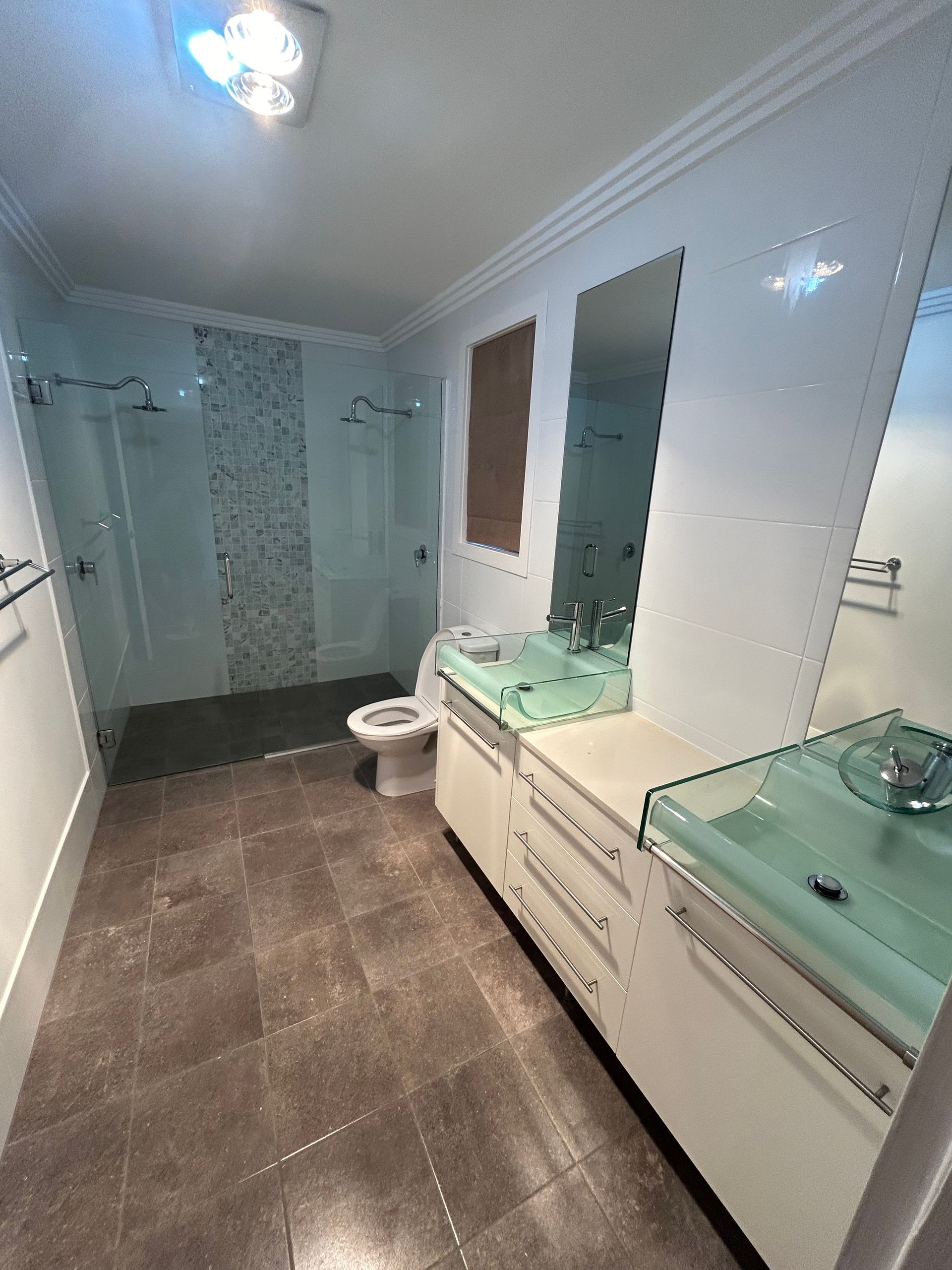 Bathroom with white cabinets, green sinks, tile floor, and a glass shower.
