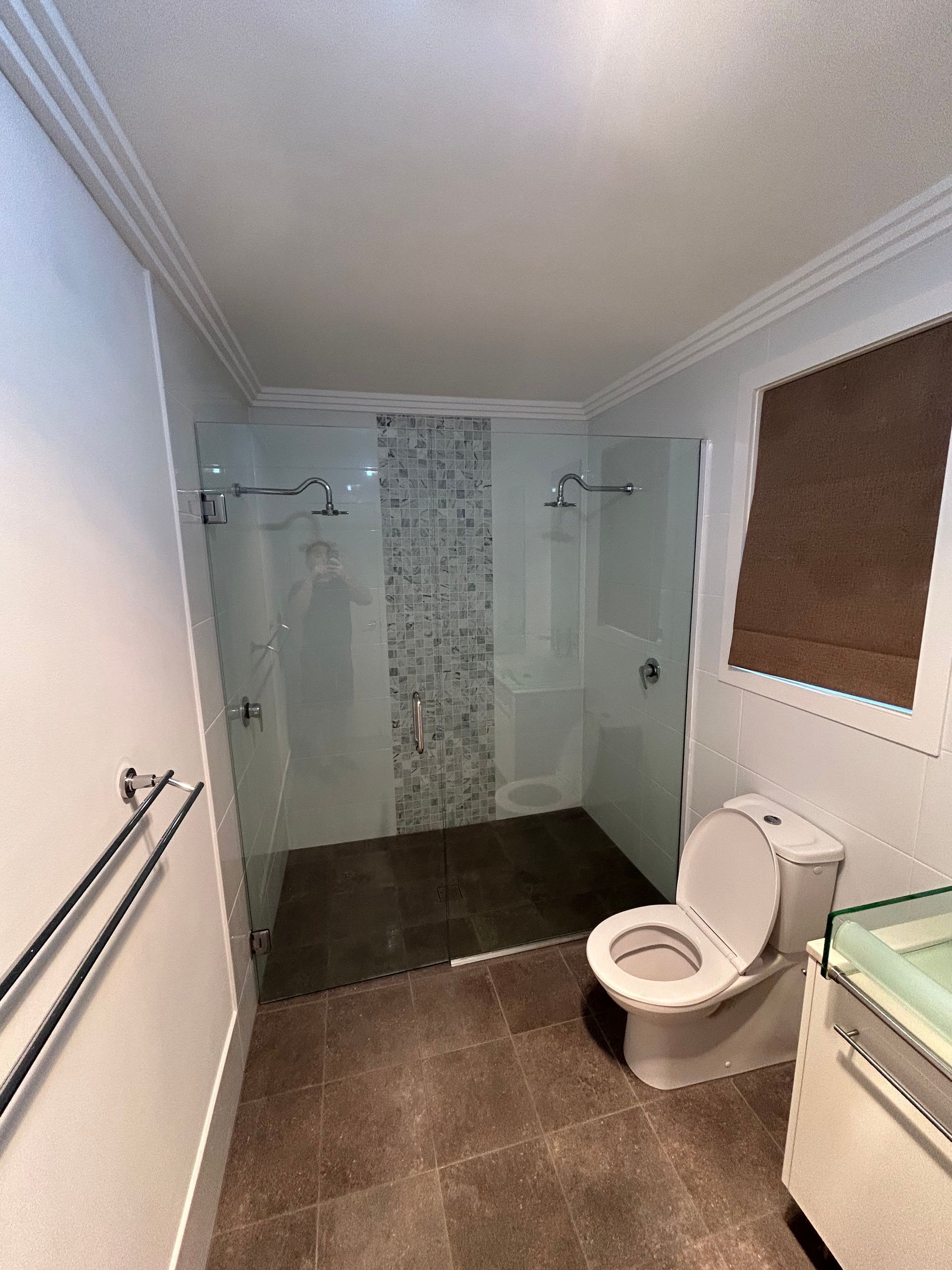 Bathroom with dual shower, toilet, and brown flooring.