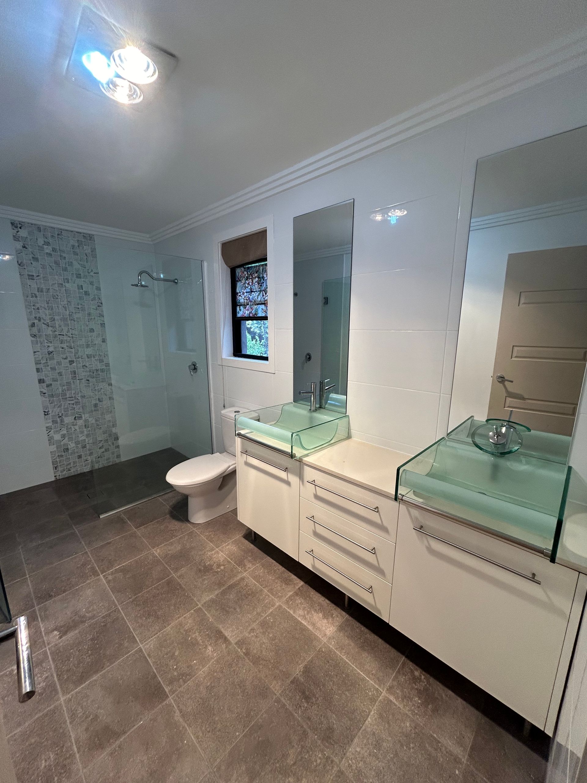 Modern bathroom with white cabinets, glass sinks, and tiled walls and floors.