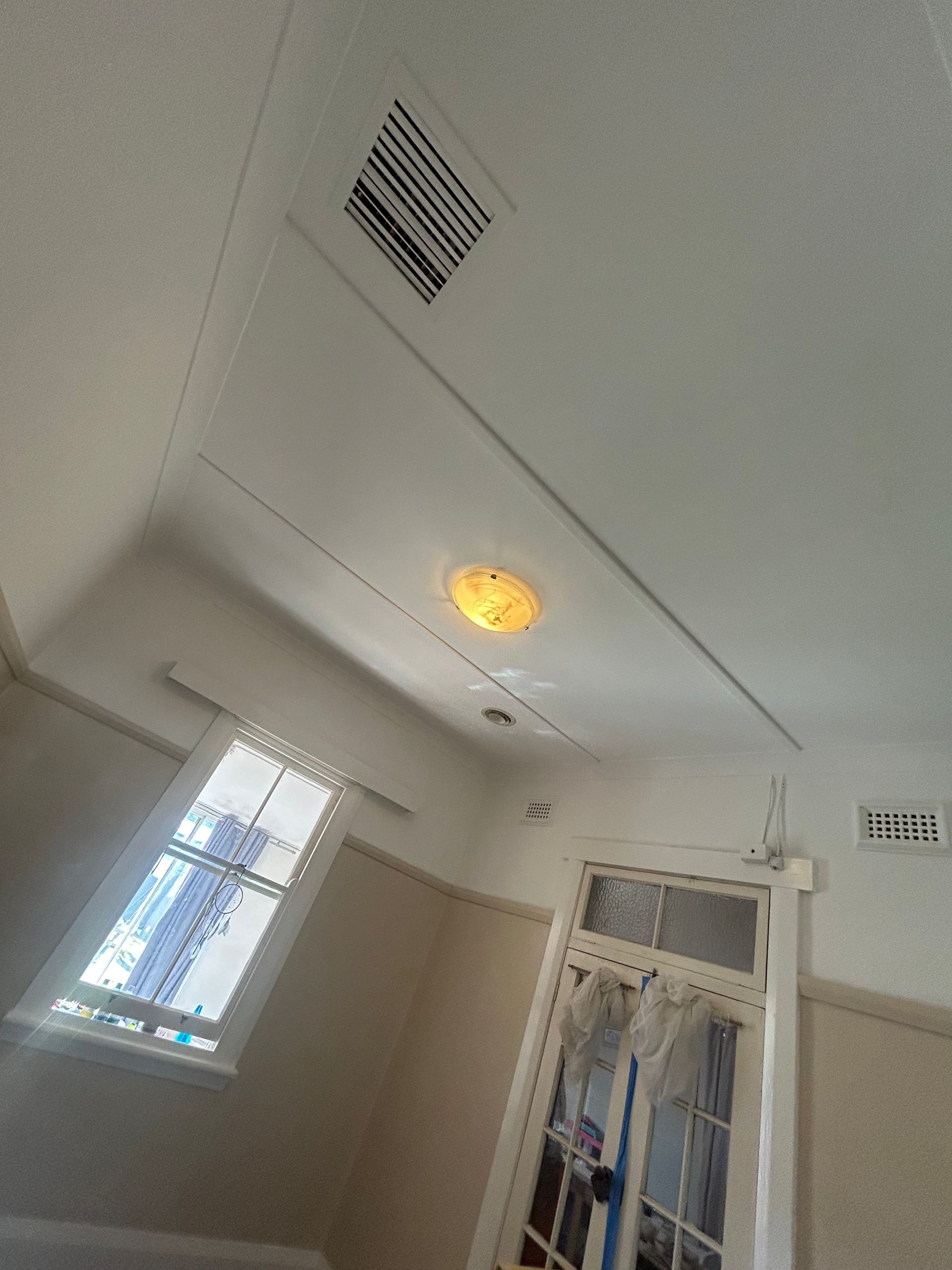 Interior room with a white ceiling, window, and a door. There is a light and a vent.