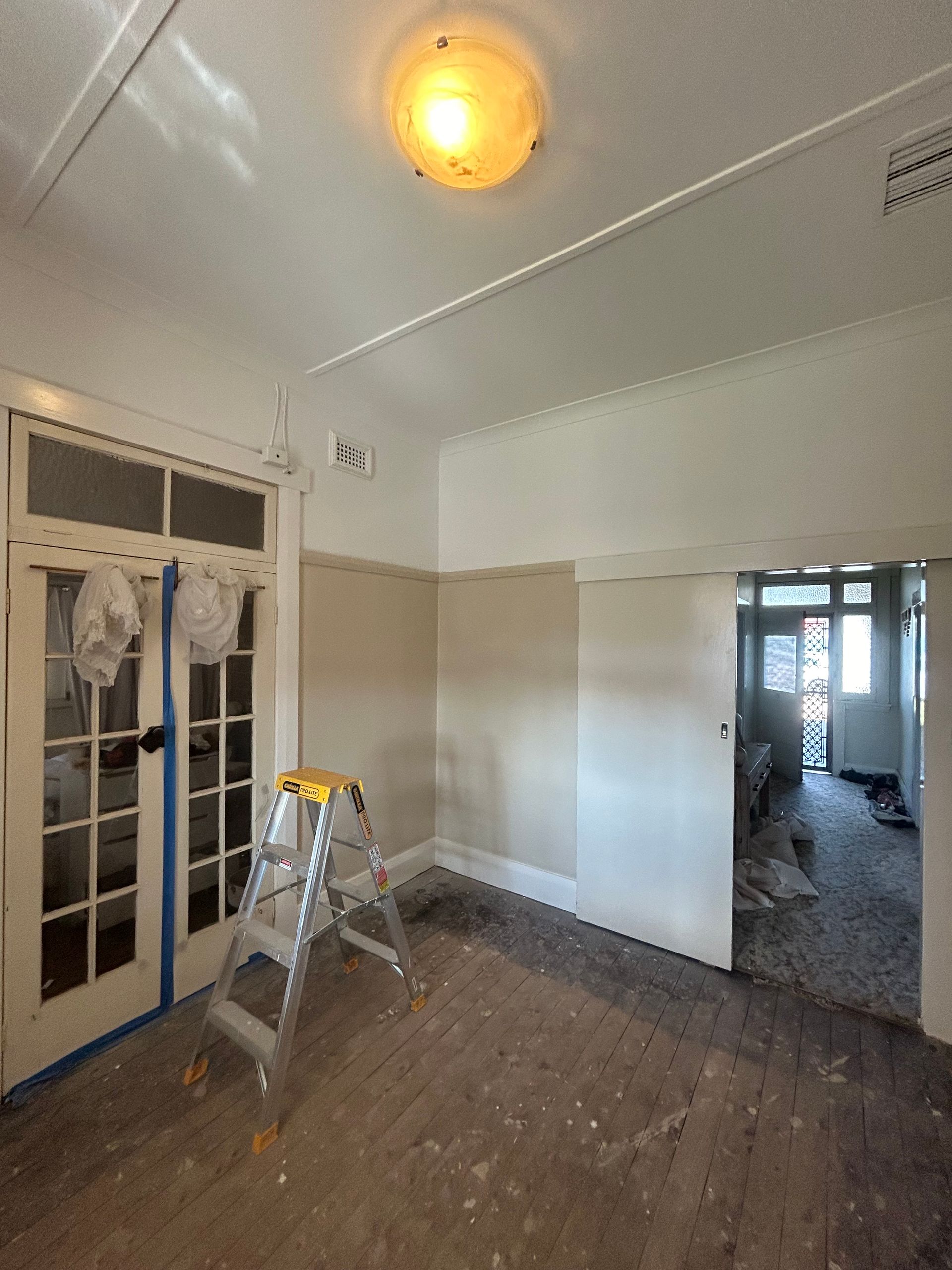 Interior of a room under renovation with a stepladder, double doors, and exposed floor.