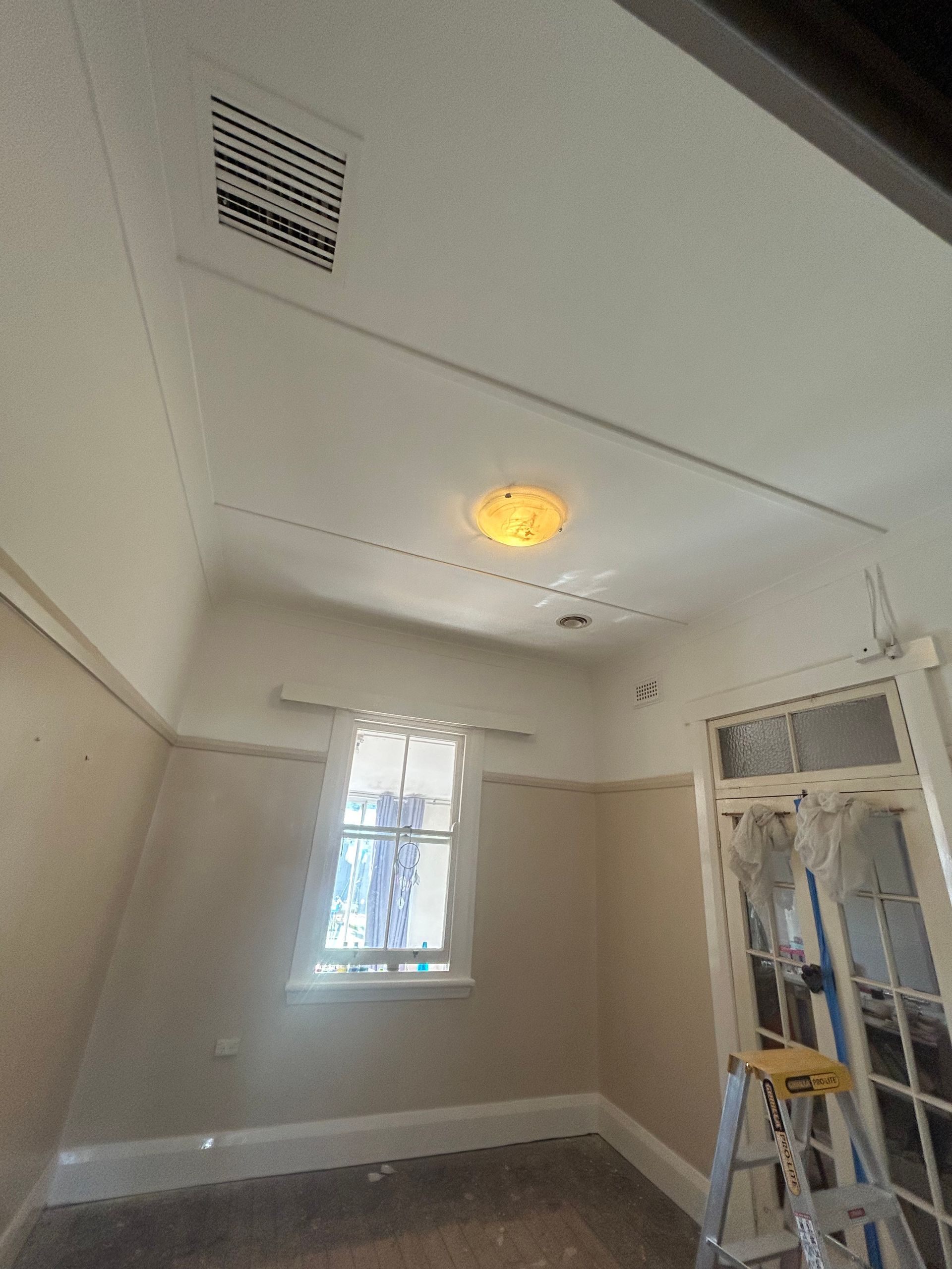 Interior room with window, ceiling vent, and a light fixture. A ladder leans against a door.