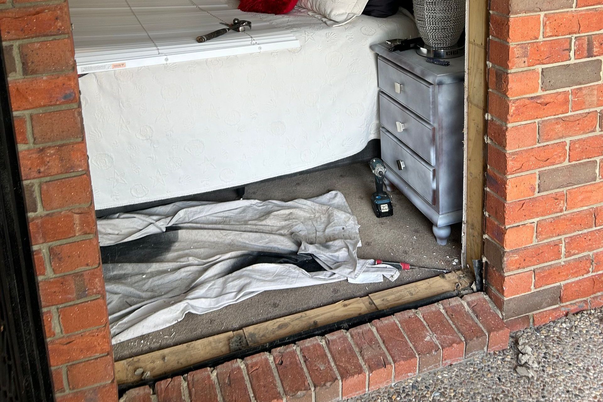 Open doorway with bed, nightstand, and tools visible. Brick exterior.