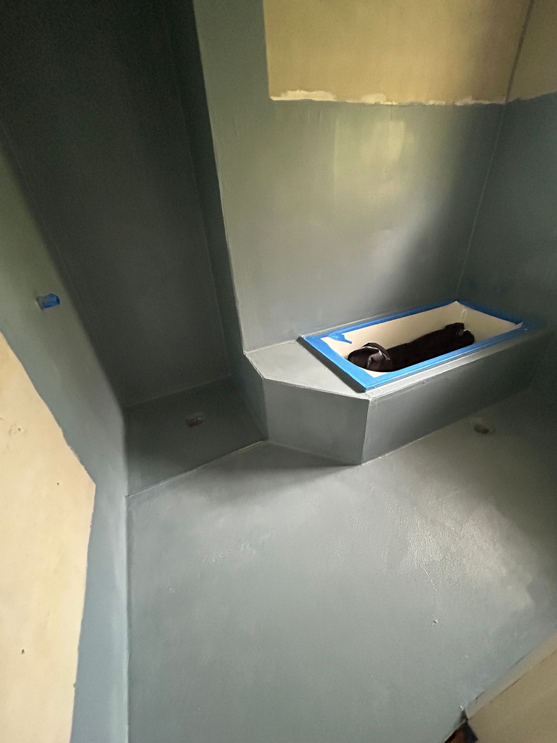 Blue-painted bathroom with a built-in tub. The walls and floor are blue-gray, with the tub's edge outlined in blue.