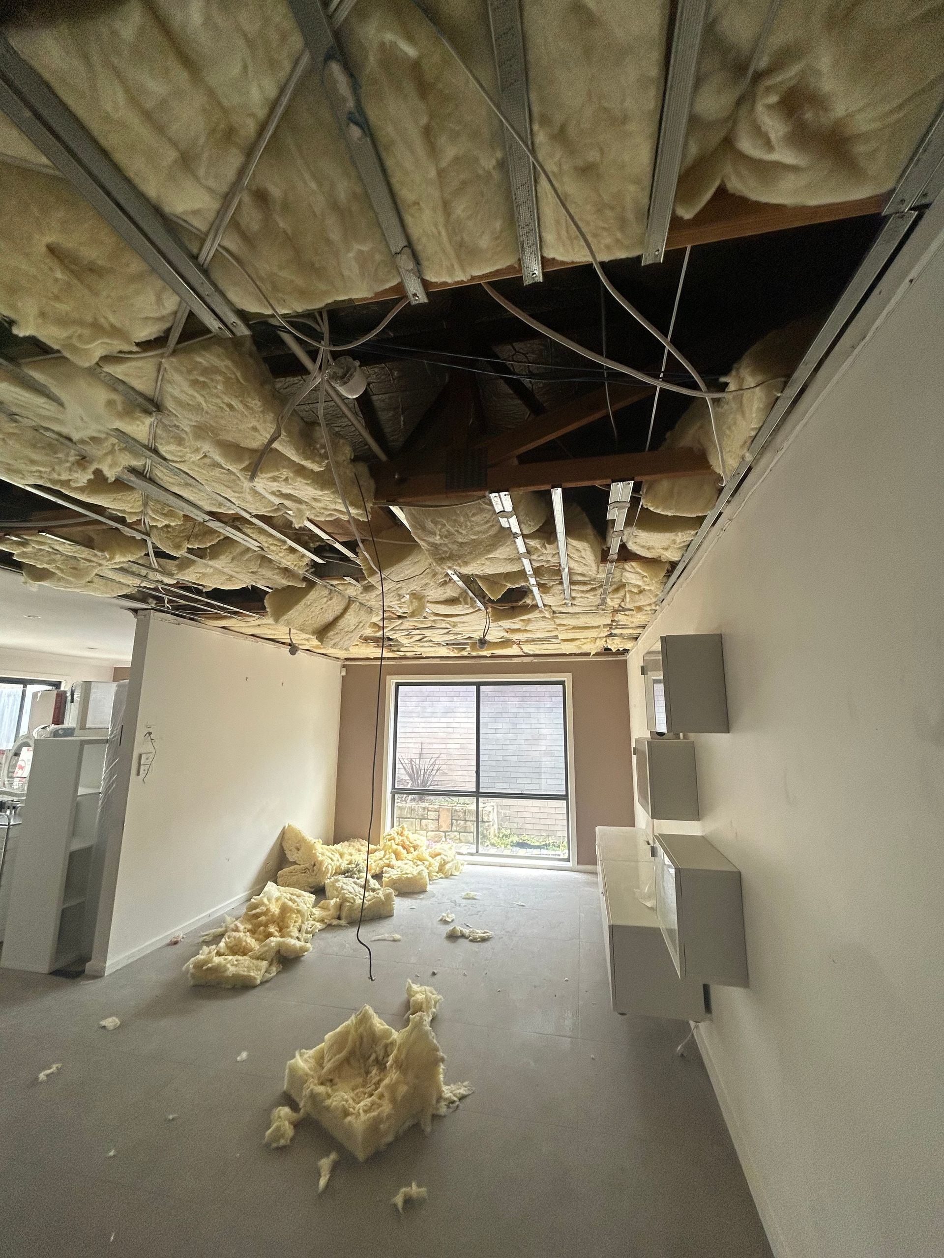 Ceiling collapse in a room with exposed insulation, scattered debris, and an exterior window.