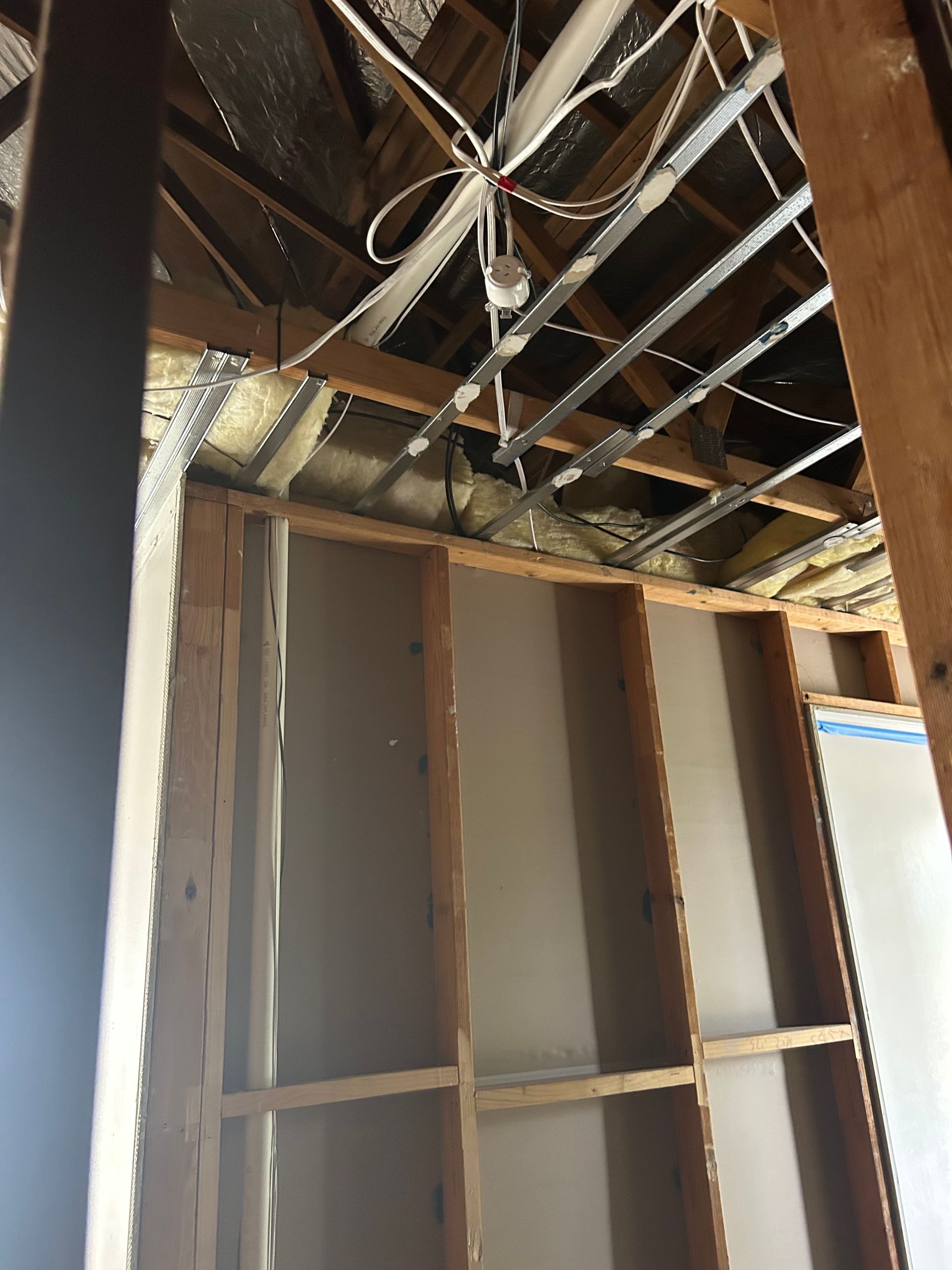 Interior view of exposed wall studs and ceiling beams, with wiring and insulation visible.