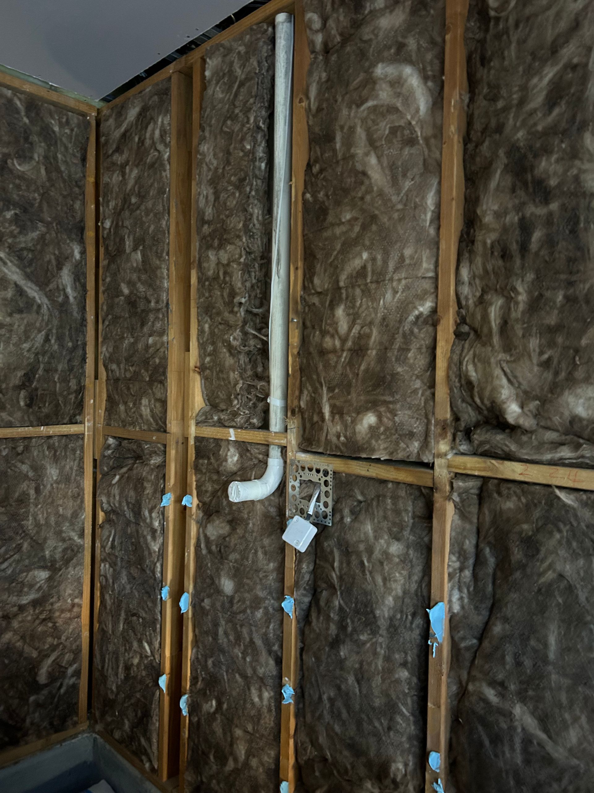 Interior wall construction with insulation, plumbing, and electrical box. Brown and white tones.