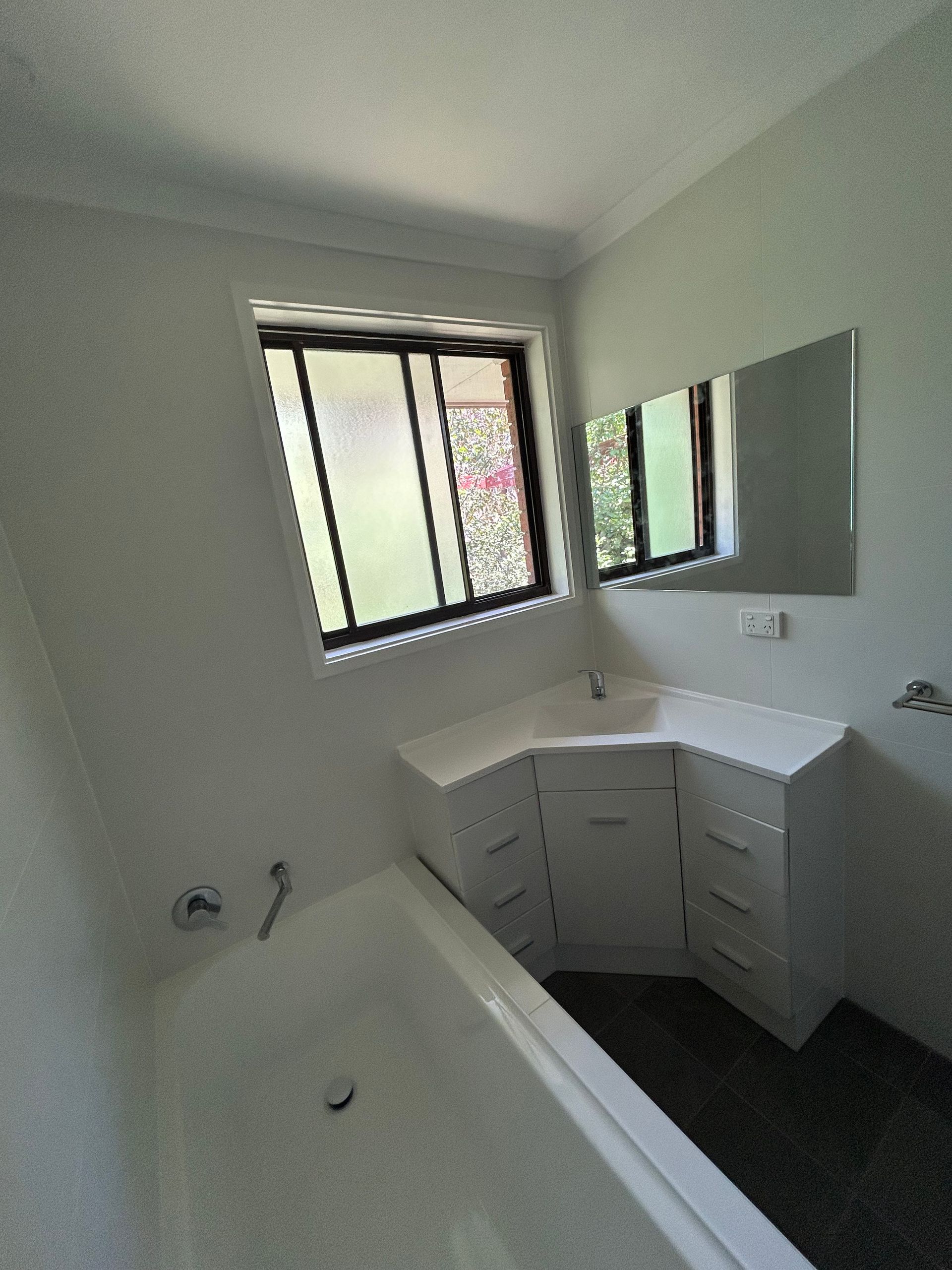 Bathroom with white fixtures, a window, corner vanity, and a tub.