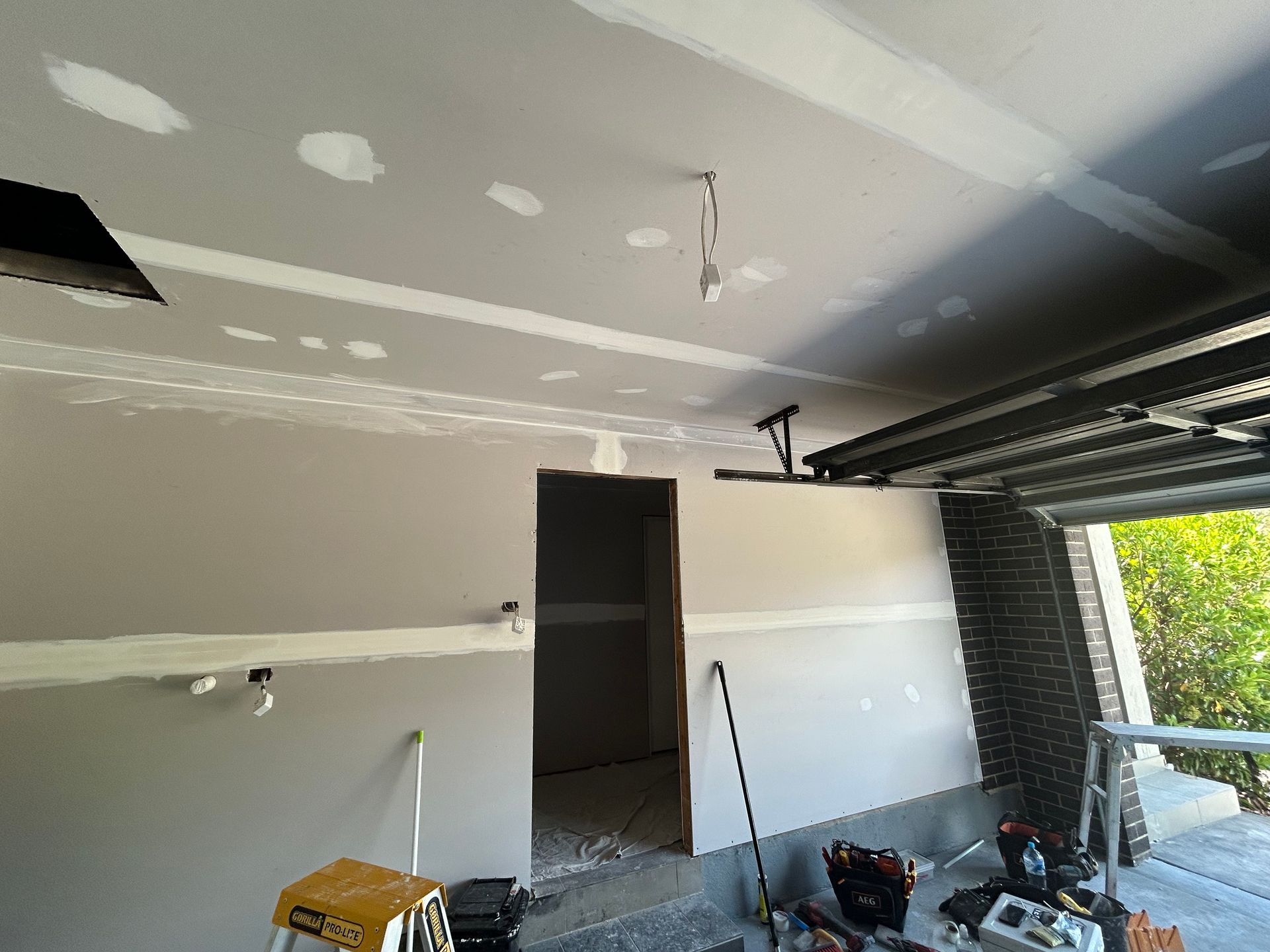 Interior view of unfinished construction; drywall on ceiling and walls. Doorway and hanging light fixture visible.