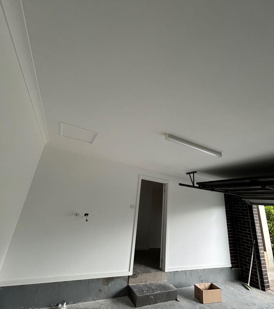 White-painted garage interior with a door, light fixture, and an open garage door on the right.