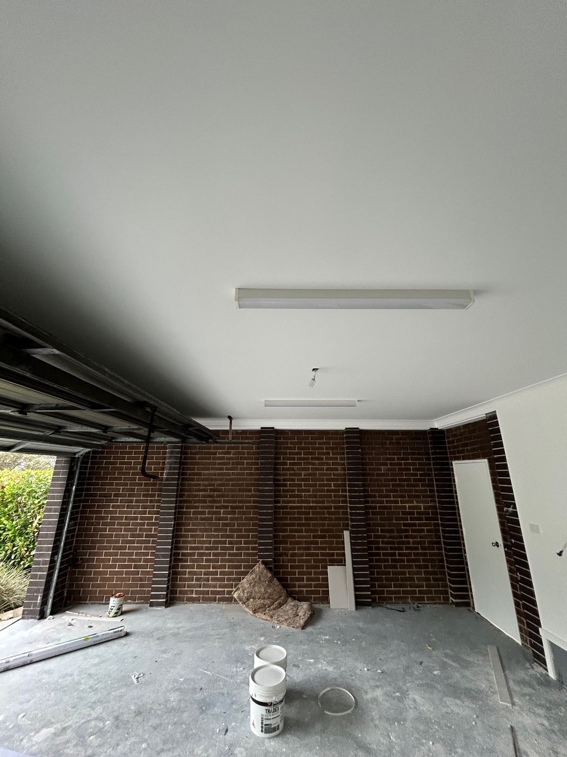 Interior view of a garage under renovation with exposed brick walls, gray floor, white ceiling, and a fluorescent light.