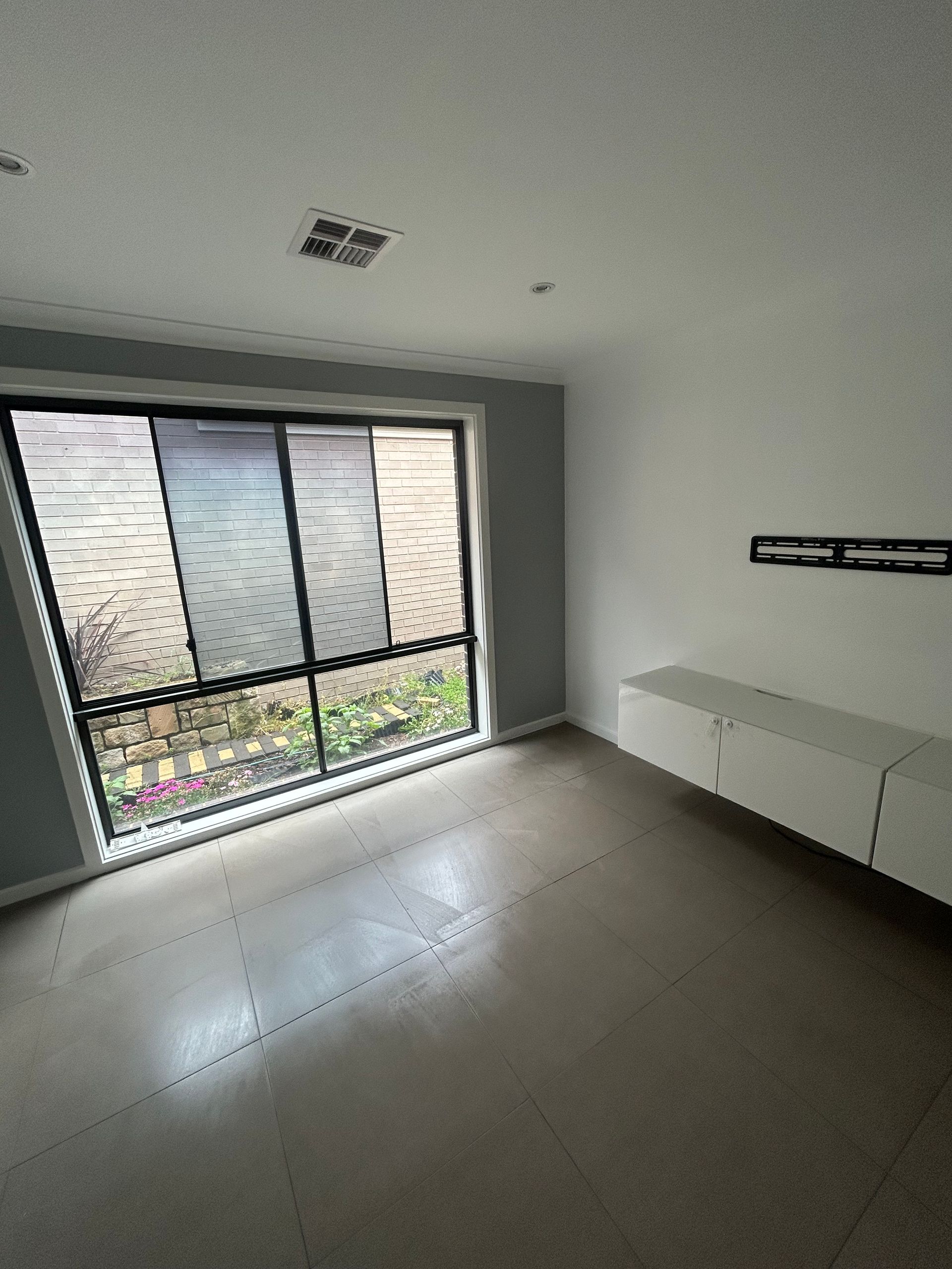 Empty living room with large window, white cabinets, and gray walls.