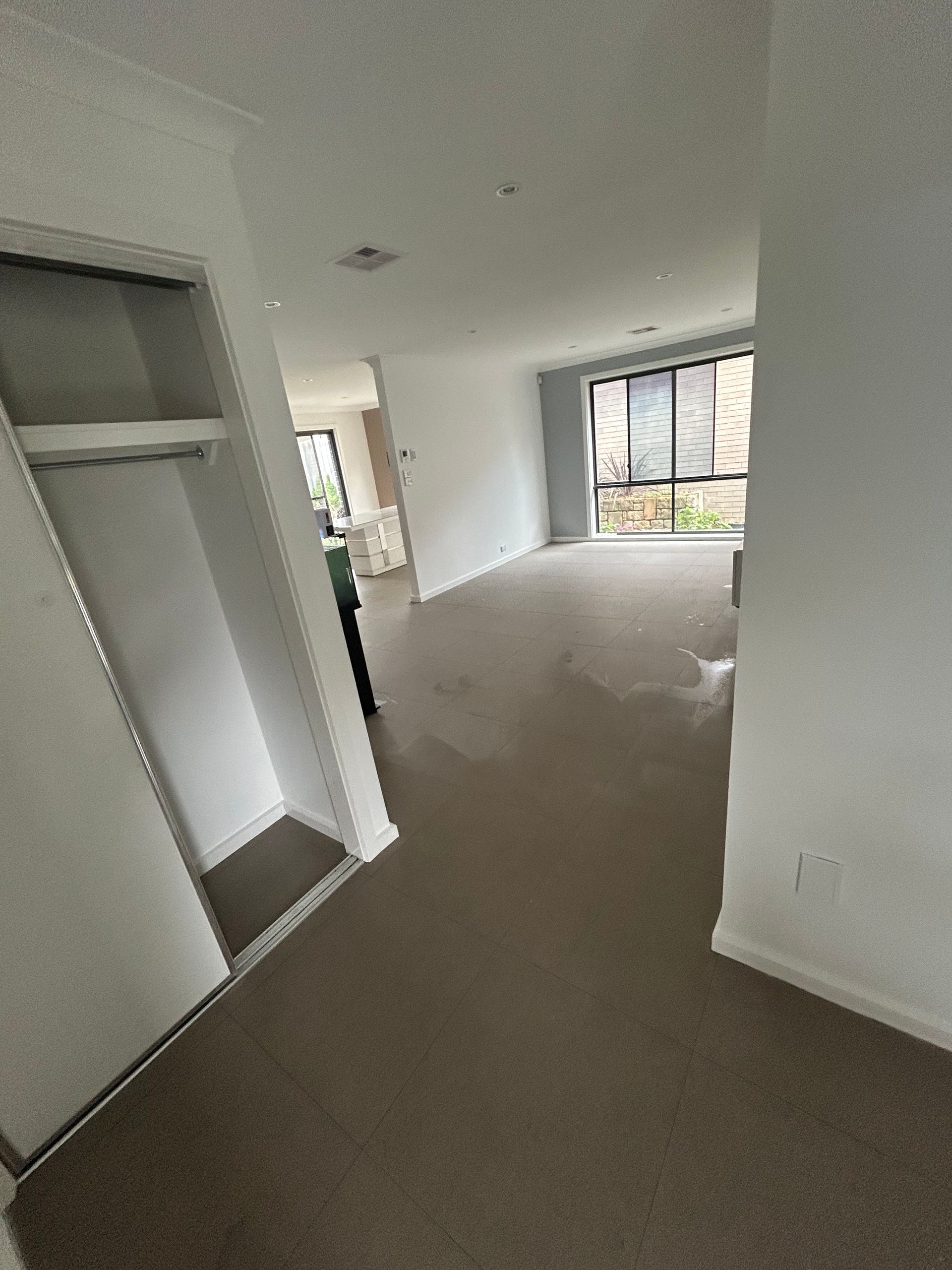 Empty room with light-colored walls and dark carpet. Closet on the left and windows at the end.