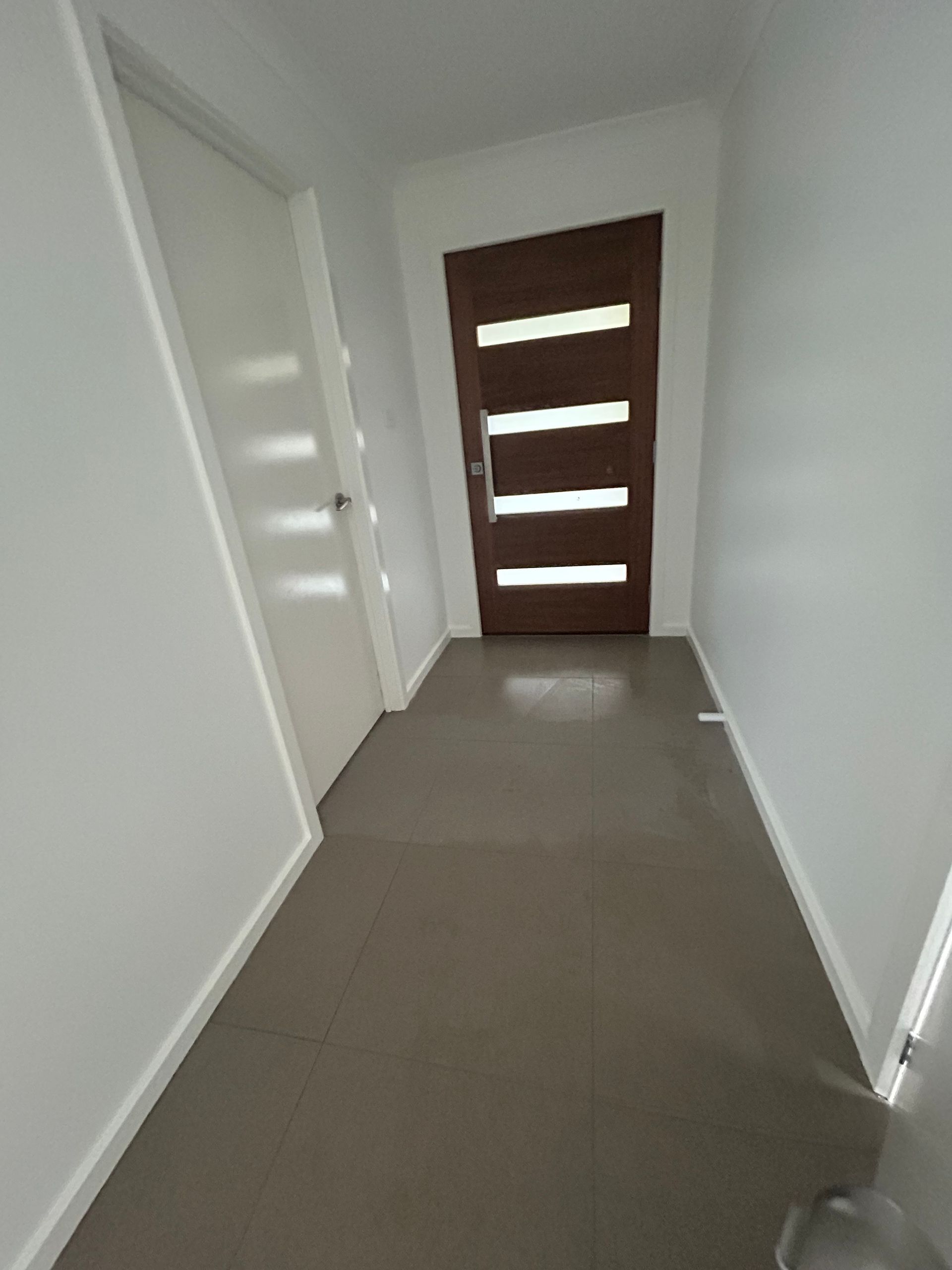 Narrow hallway with brown door and white walls; tiled floor.