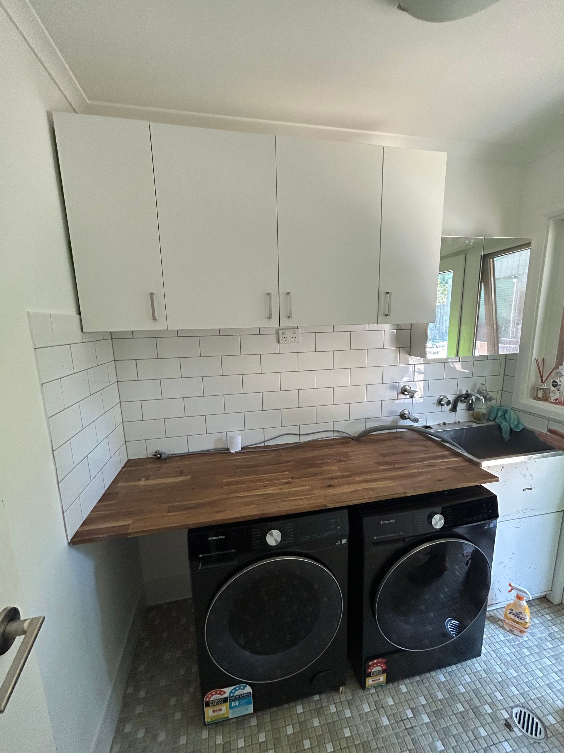 Laundry room with white cabinets, dark washer/dryer, wooden countertop, and sink.
