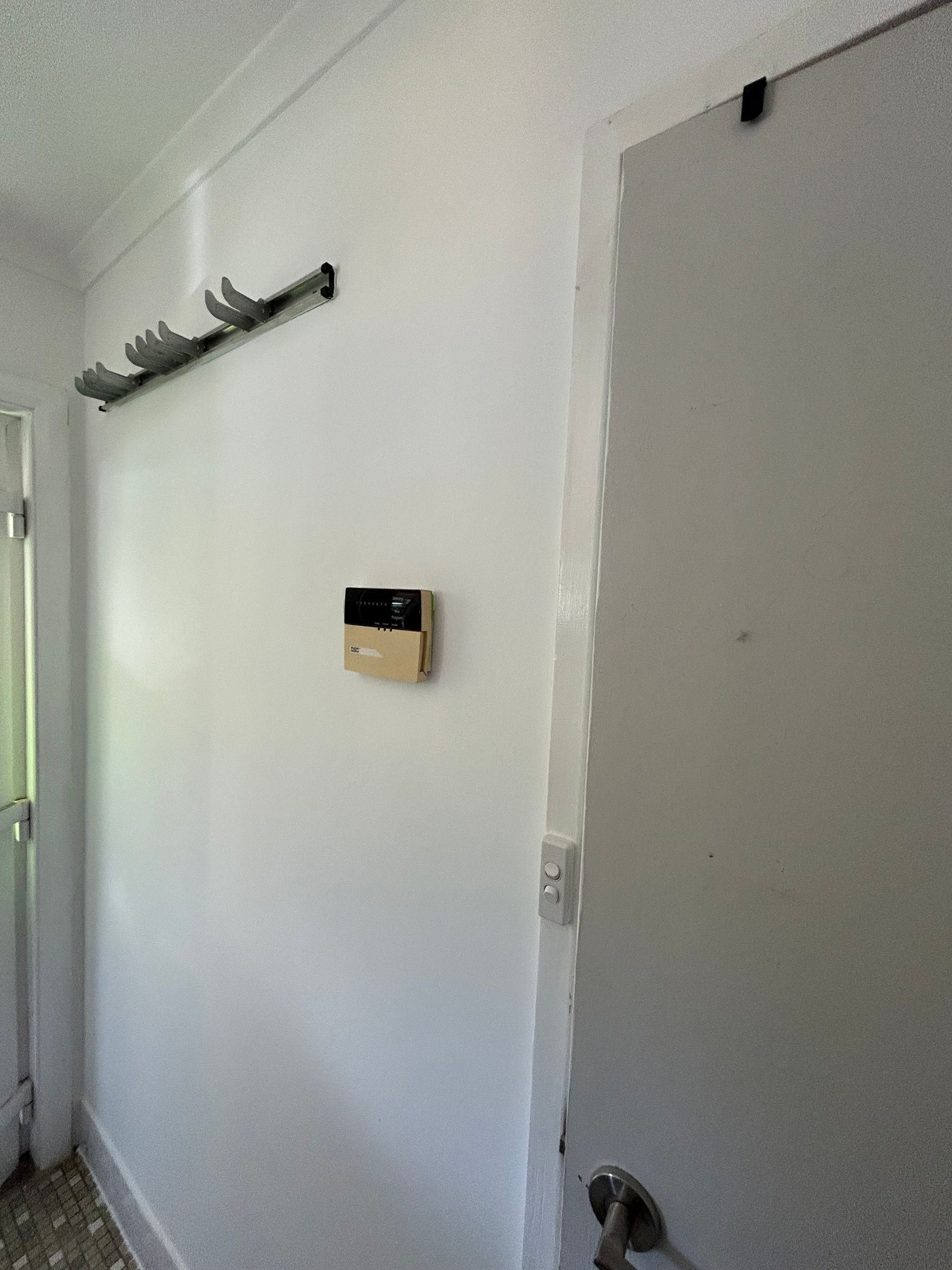 White hallway with coat rack, security panel, and closed door.