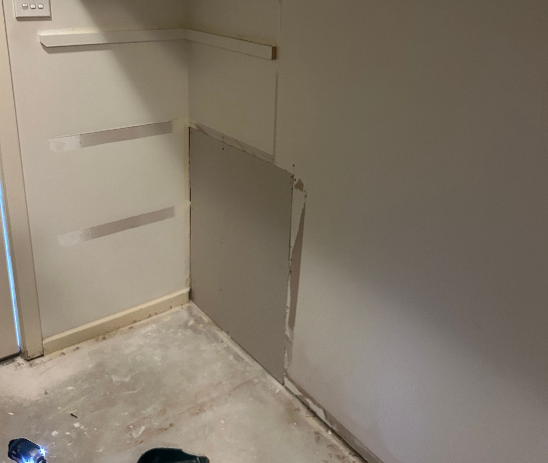 A partially installed drywall panel in a corner, with tape, in a room with concrete floor.