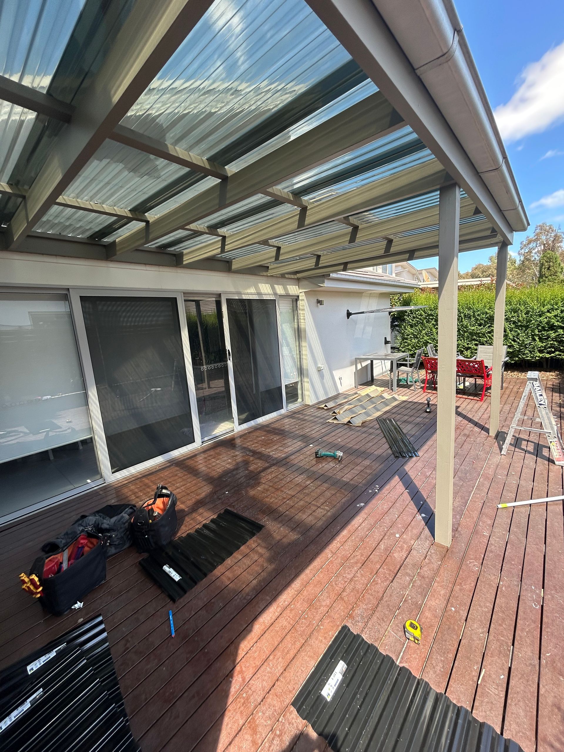 Deck with corrugated roof, tools, and sliding glass doors. Overcast day.