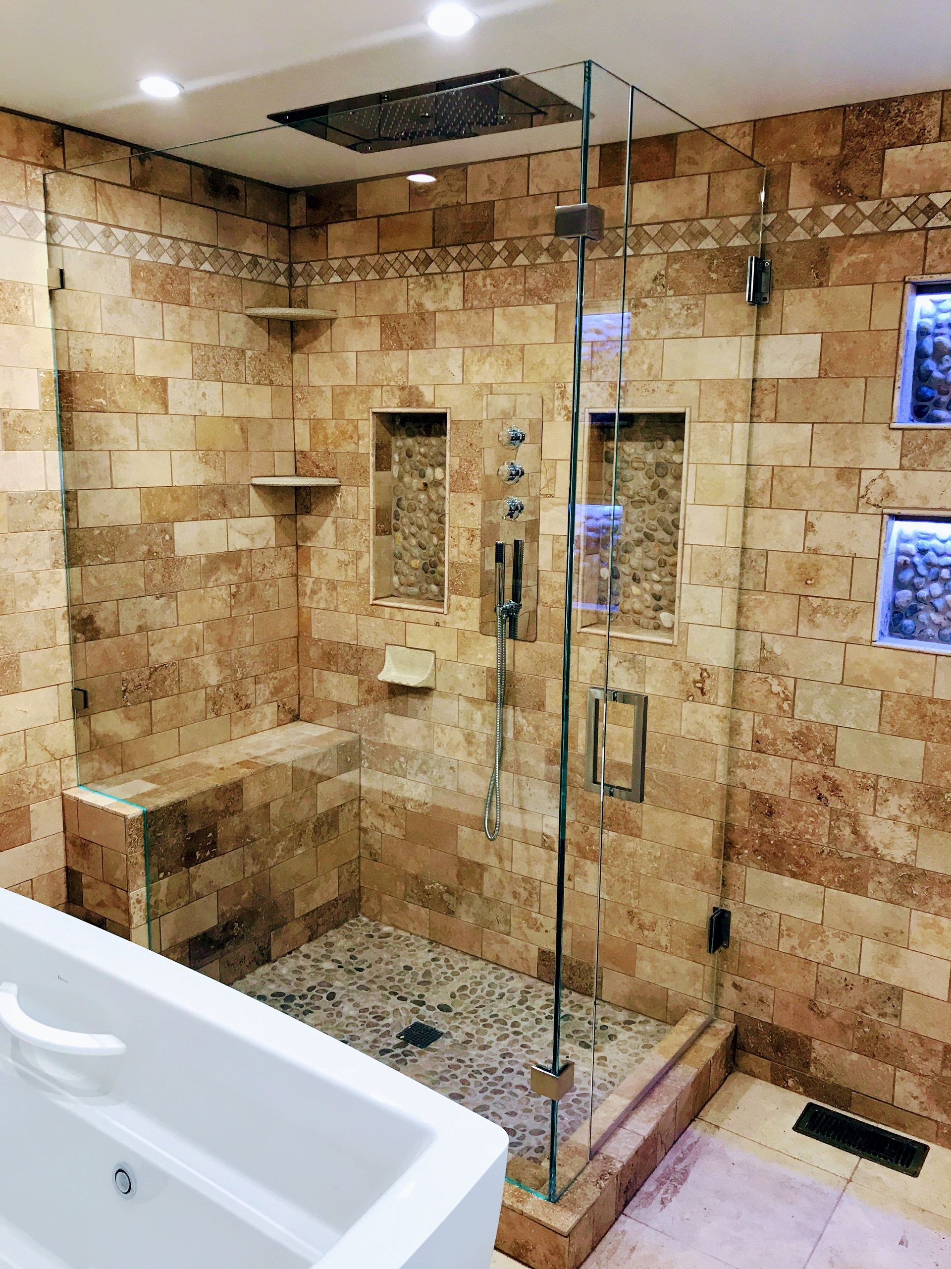 Bathroom with stone walls, glass shower door, and pebble floor.