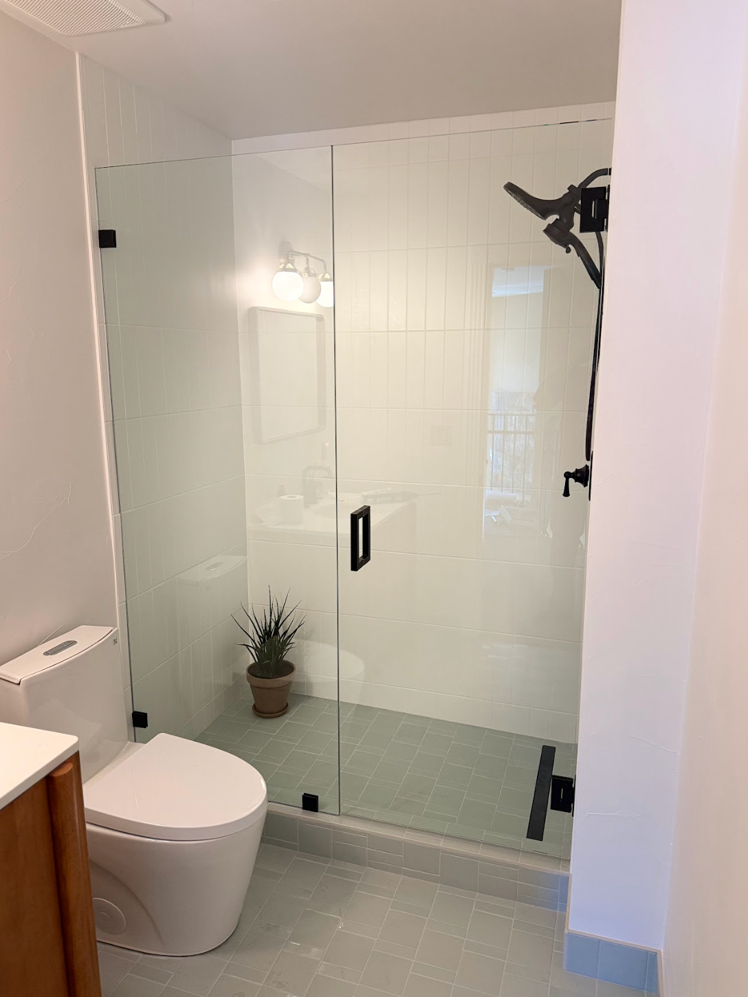 A modern bathroom featuring a white toilet next to a glass-enclosed walk-in shower with matte black fixtures.