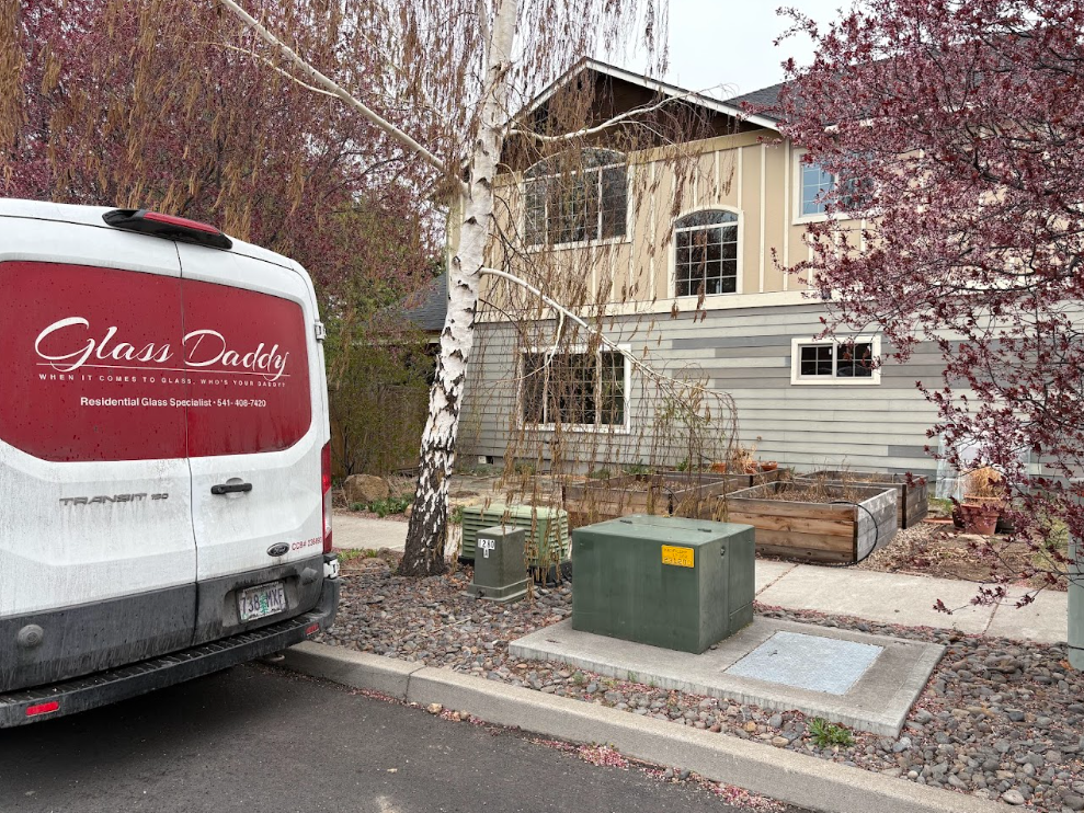 A white van parked beside a two-story house with autumn trees and a green utility box in front.
