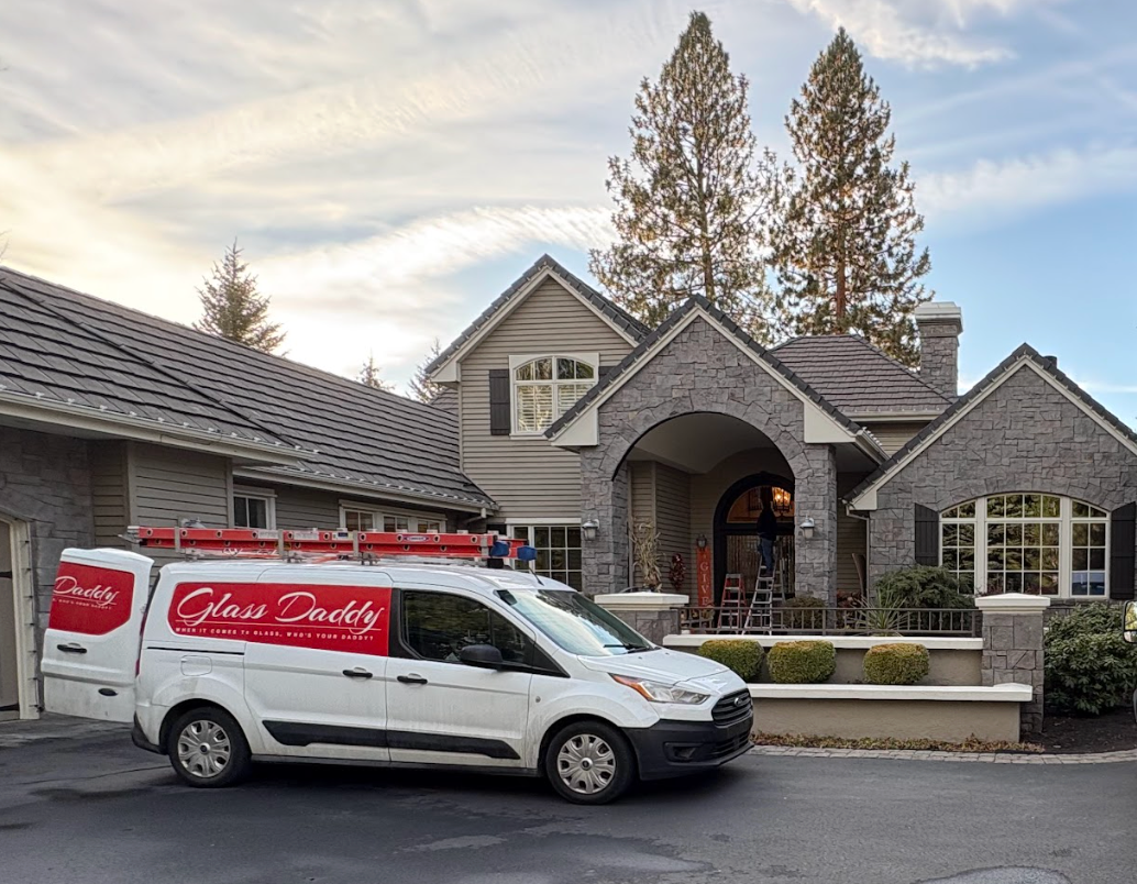 White service van parked in front of a gray house with stone arches and tall trees