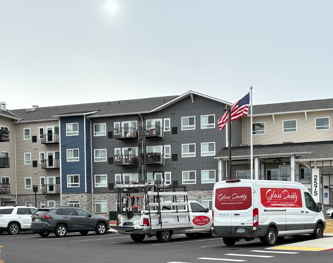 Parked Coca-Cola delivery trucks in front of an apartment building with an American flag.