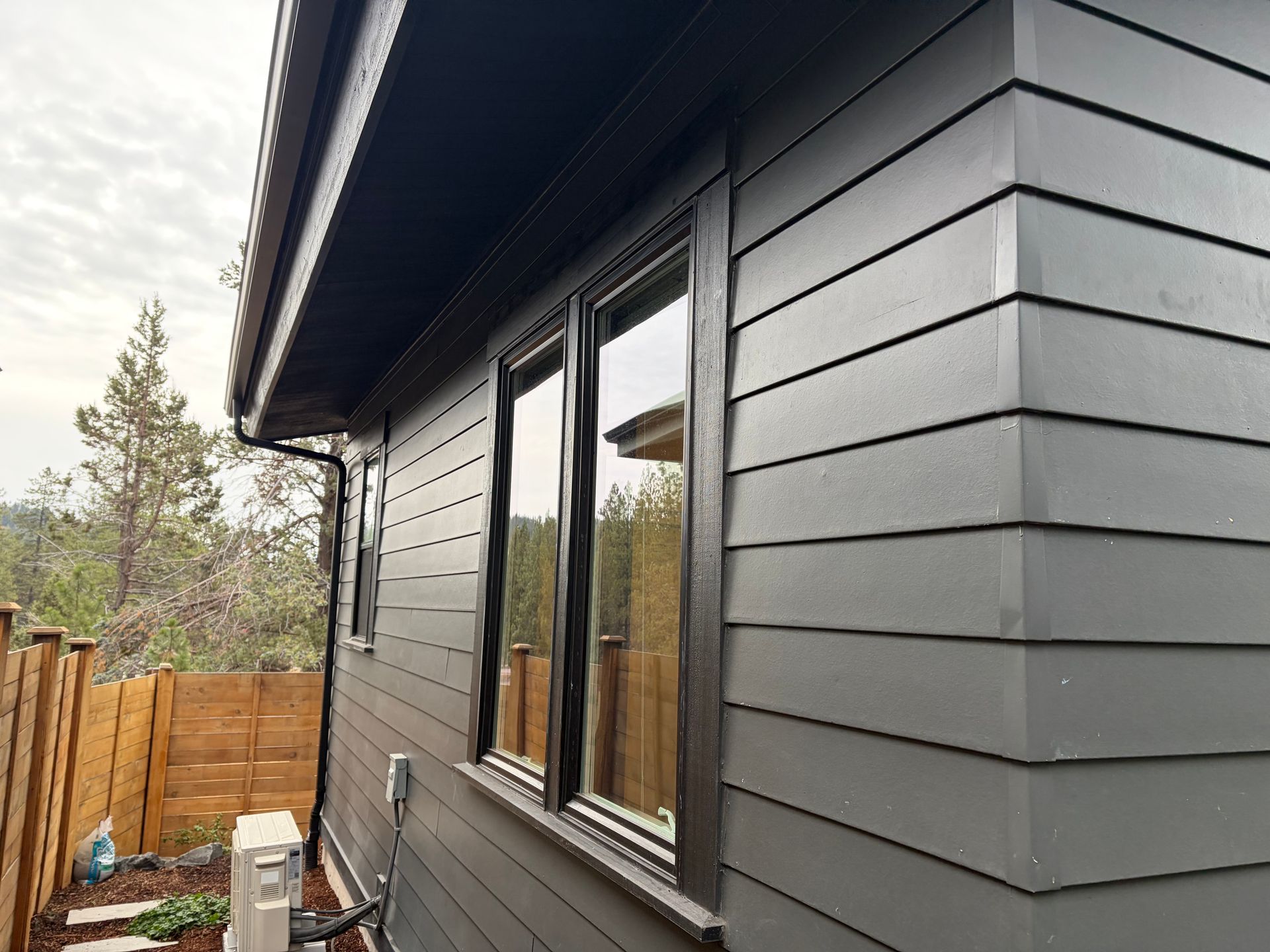 Modern gray house exterior with black trim, windows, and a wooden fence on the side yard