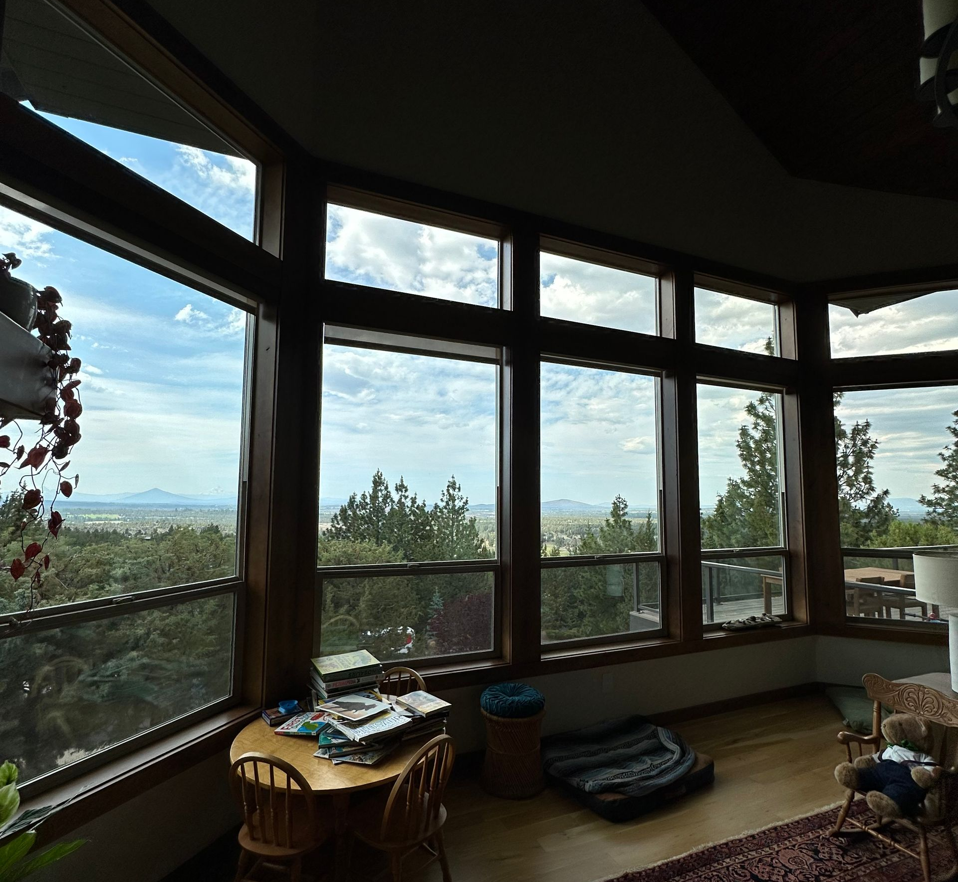 Large windows in a room overlook a vista of trees and a distant mountain range. Interior has a wooden floor and furniture.
