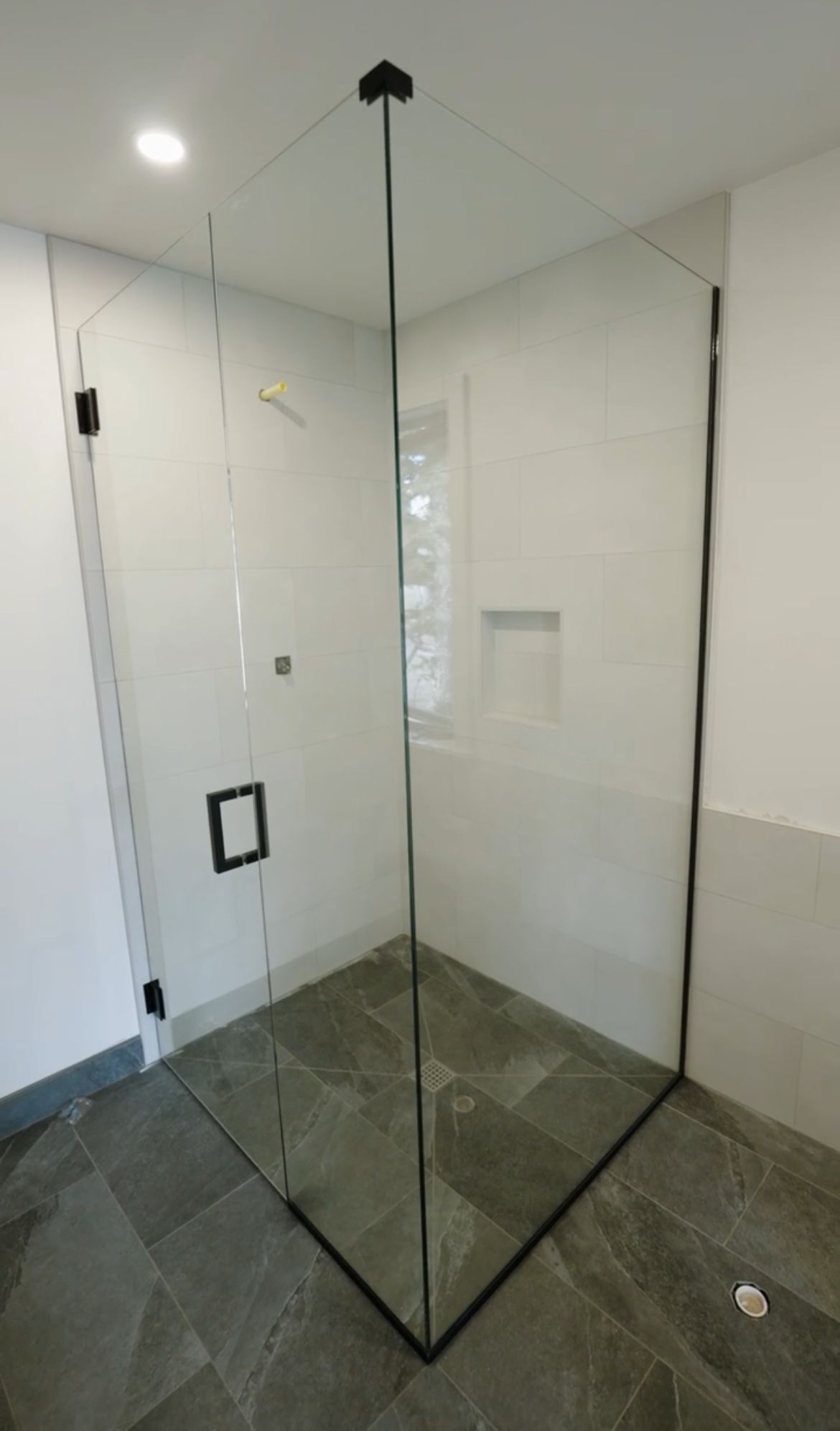 Corner glass shower enclosure with black hardware and gray tile floor.