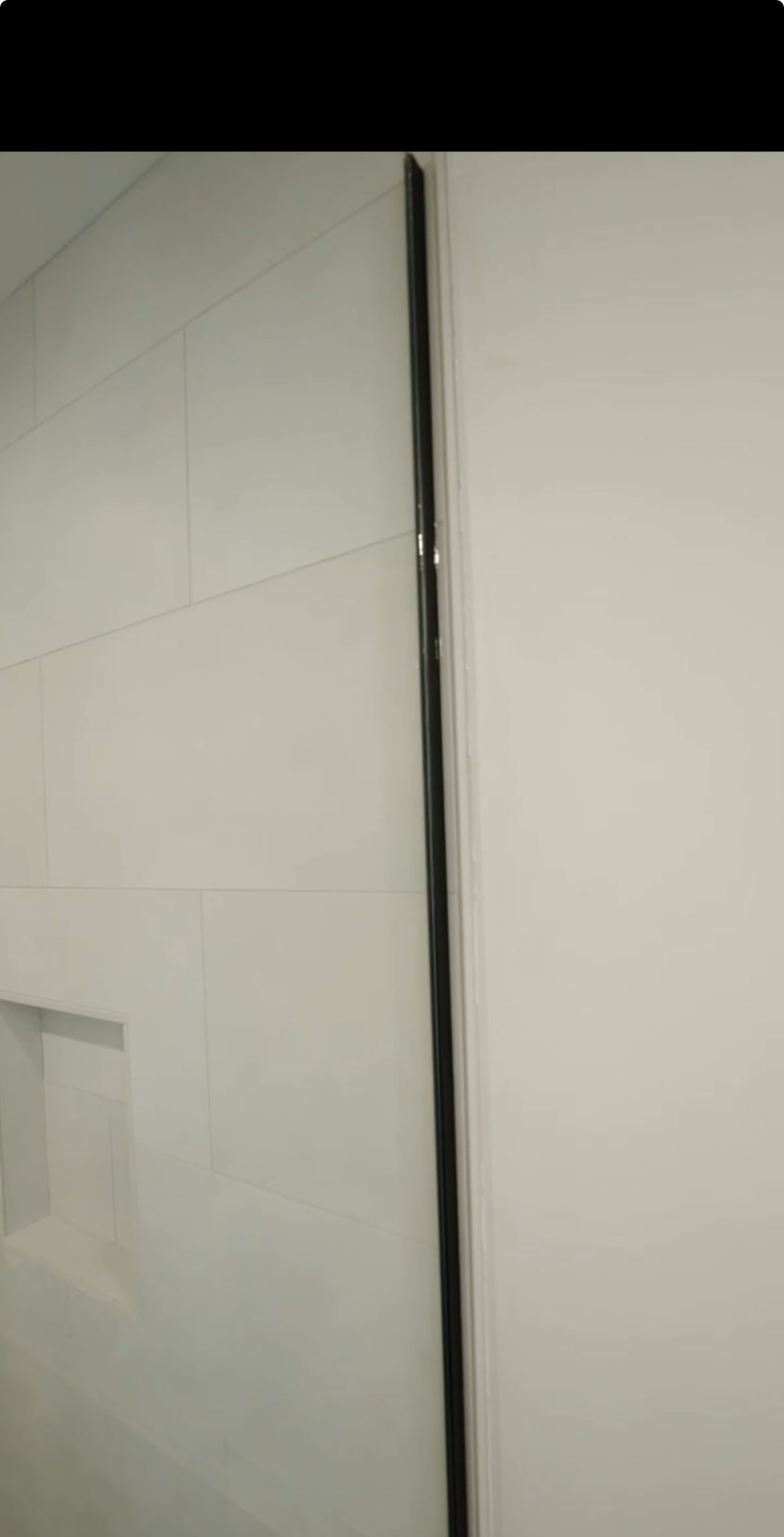White tiled wall next to a plain white wall, separated by a black vertical line.