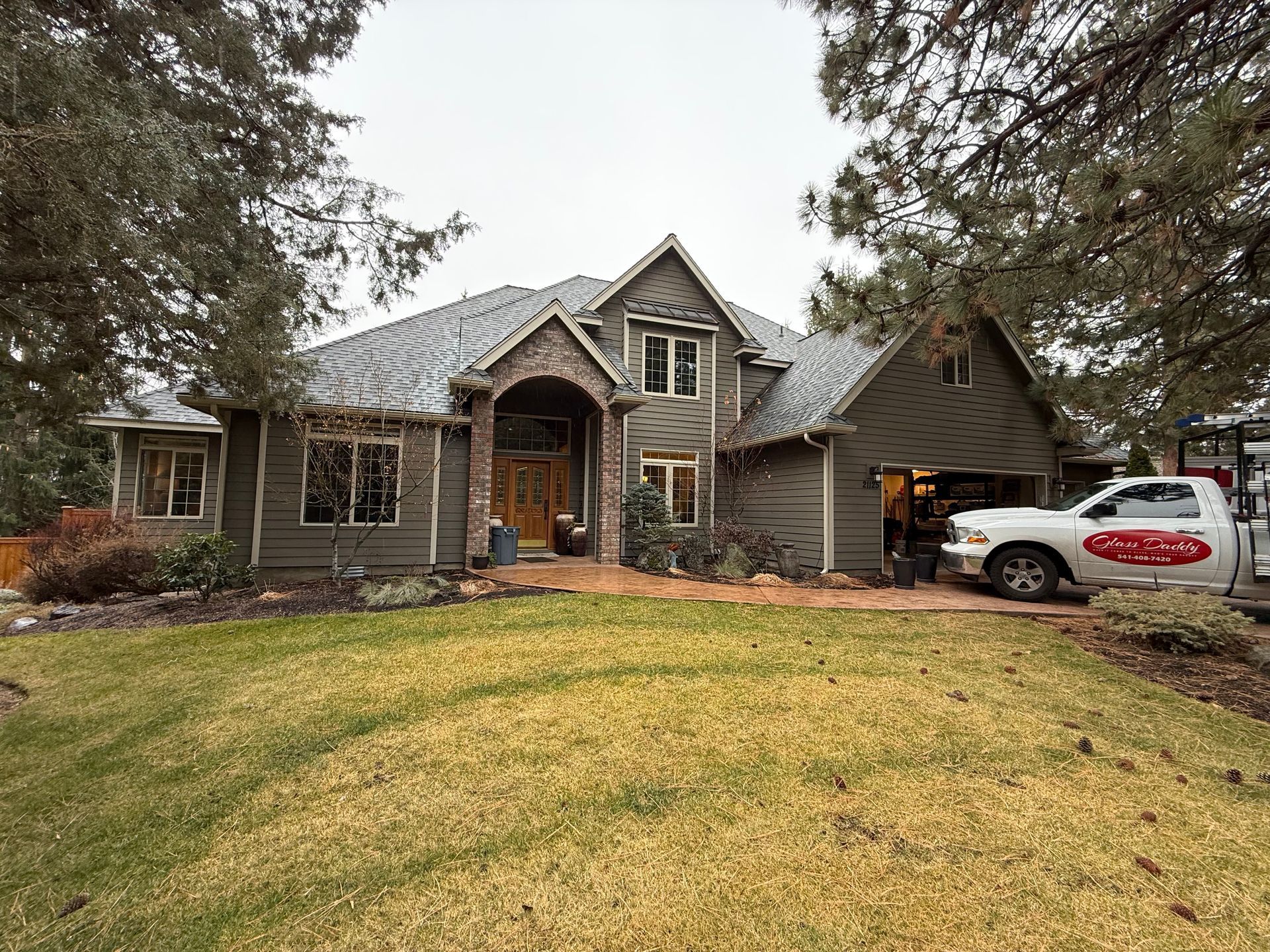 Gray house with brown brick accents, green lawn, white van parked in front.