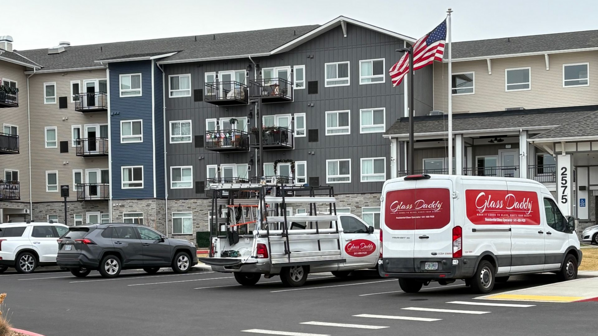 Vehicles parked in front of an apartment building, including a service van with a logo and a truck with a utility cart.