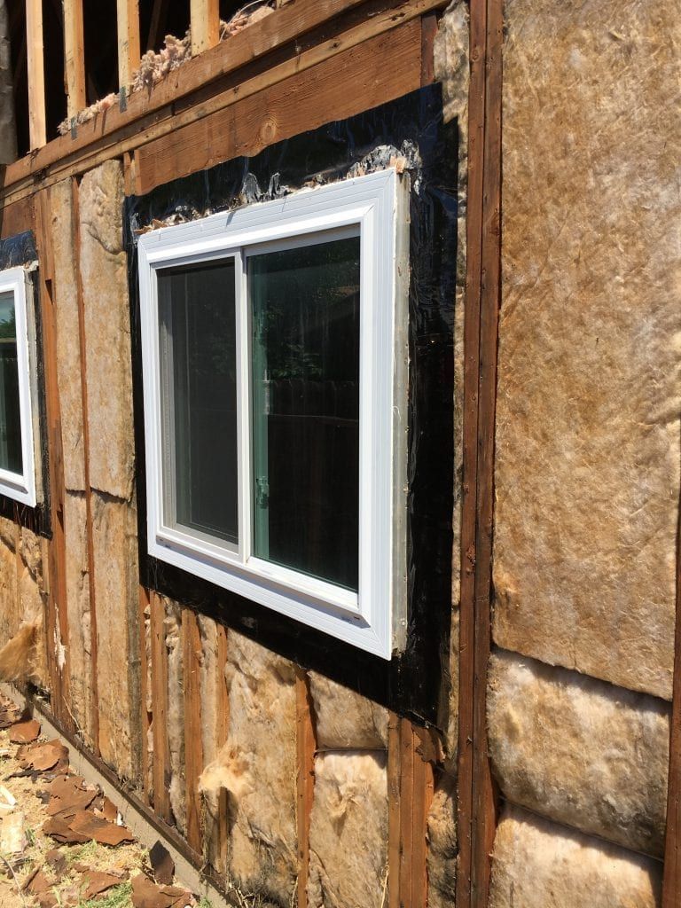 Window installation on a wooden building exterior with black flashing and insulation visible.