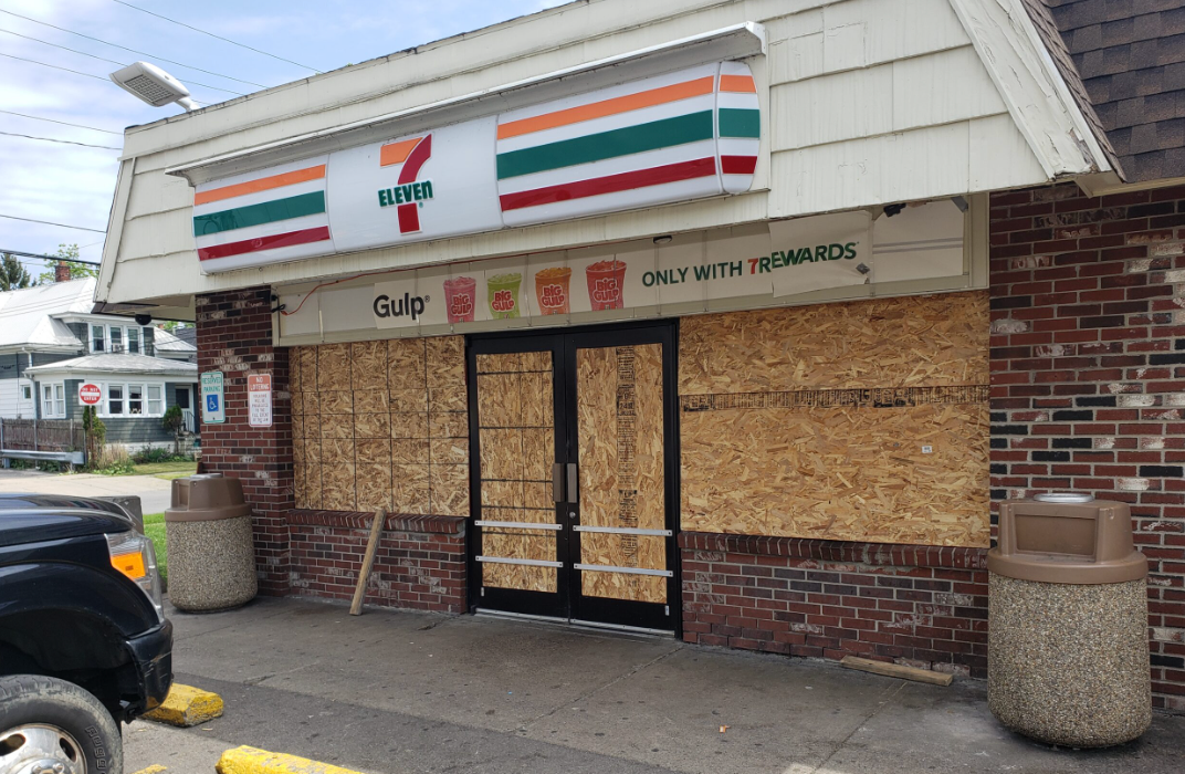 A 7 eleven store is boarded up with plywood.