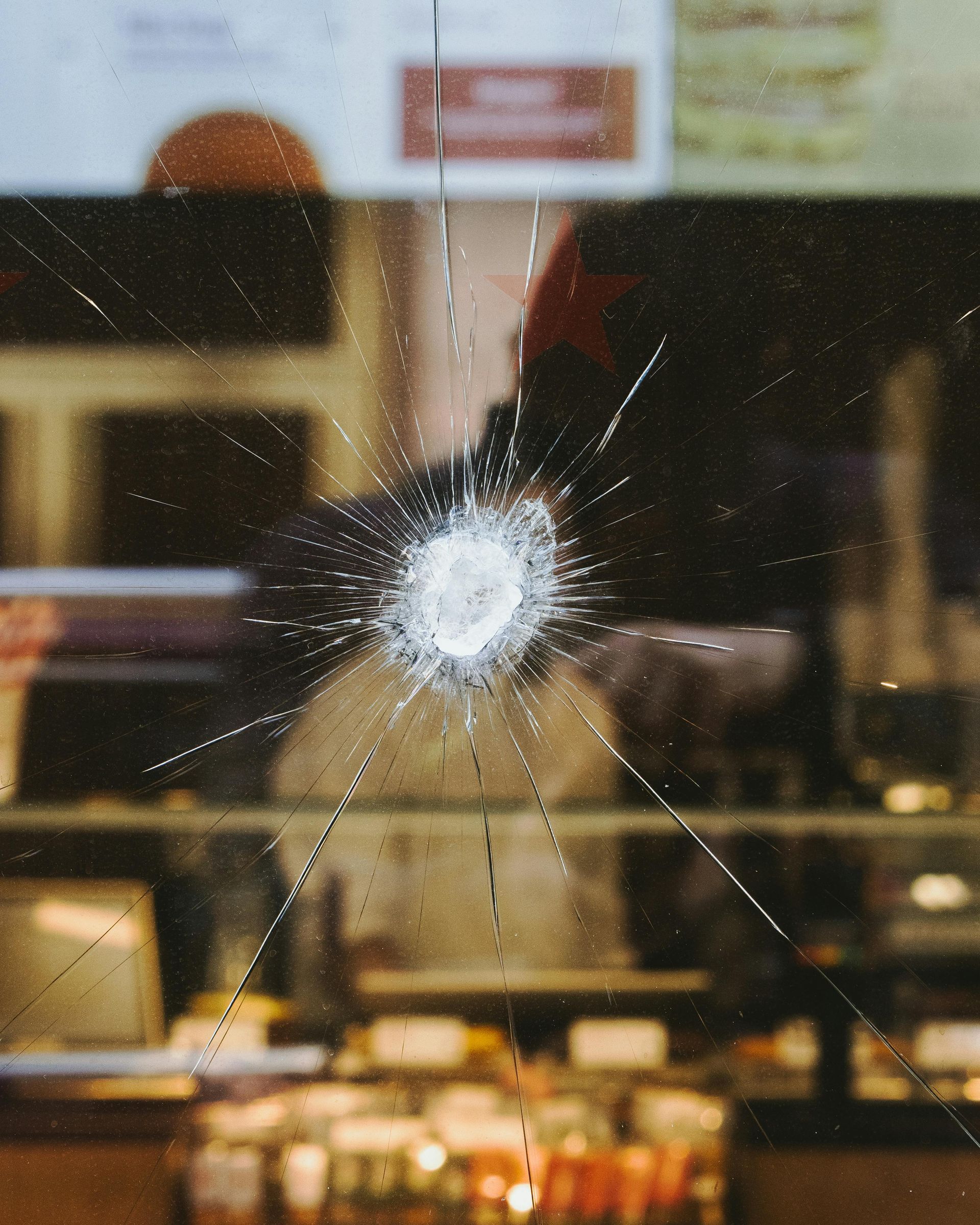 Shattered glass window with a starburst crack pattern, reflecting an interior with a person and counter.