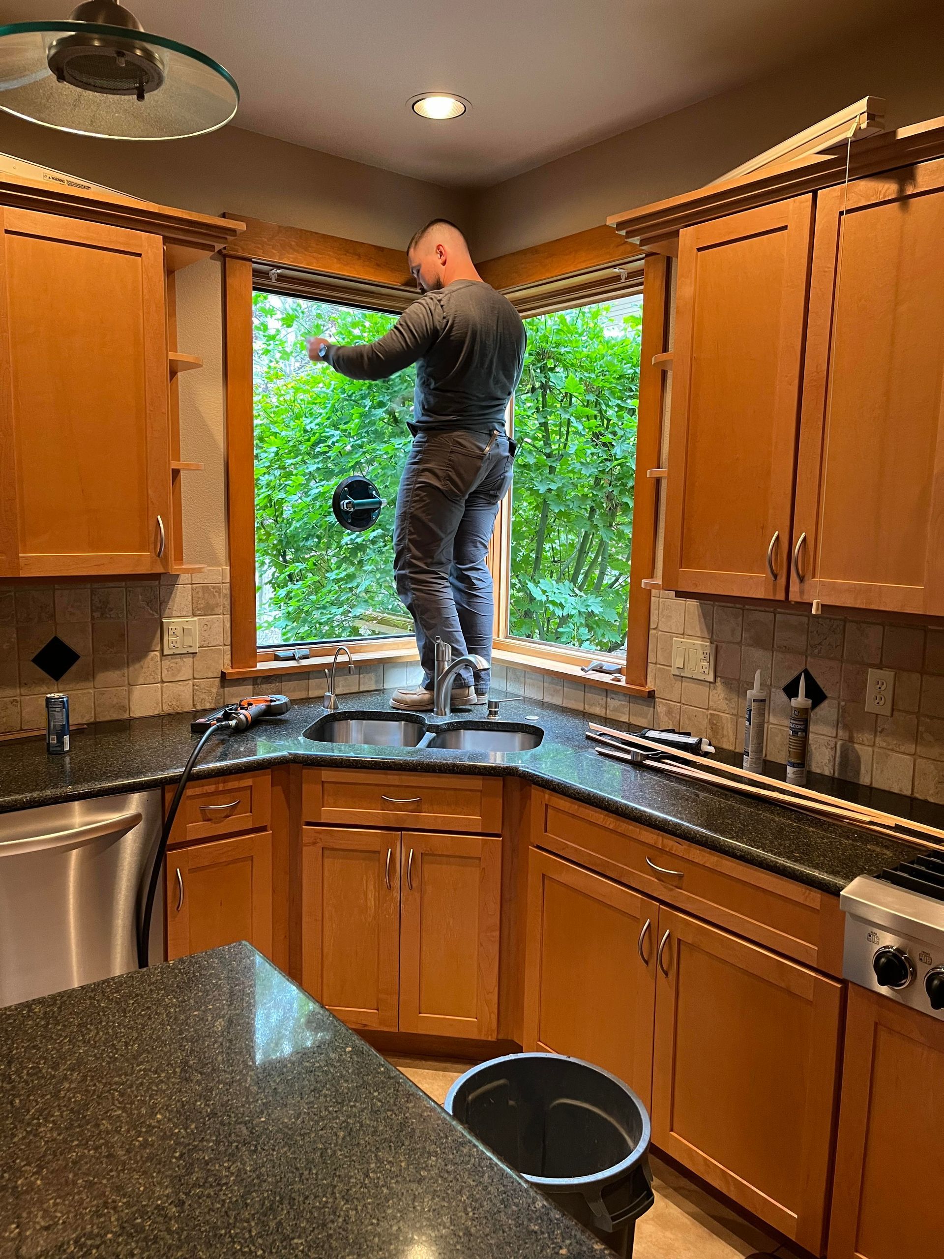 A man is standing on a counter in a kitchen fixing a window.