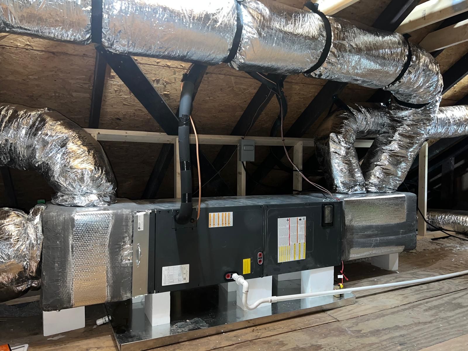 Large HVAC unit with shiny insulated ducts in an attic crawlspace
