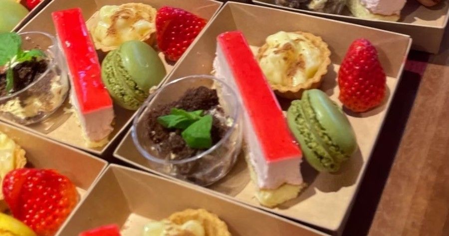 Close-up of individual dessert boxes with cheesecake, macarons, tarts, and strawberries.