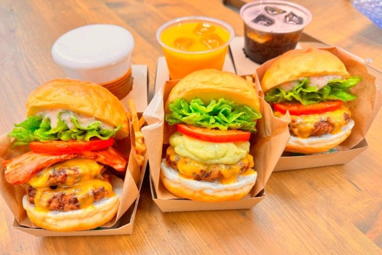 飲み物の横の木製のテーブルの上にハンバーガーが 3 つ置かれています。