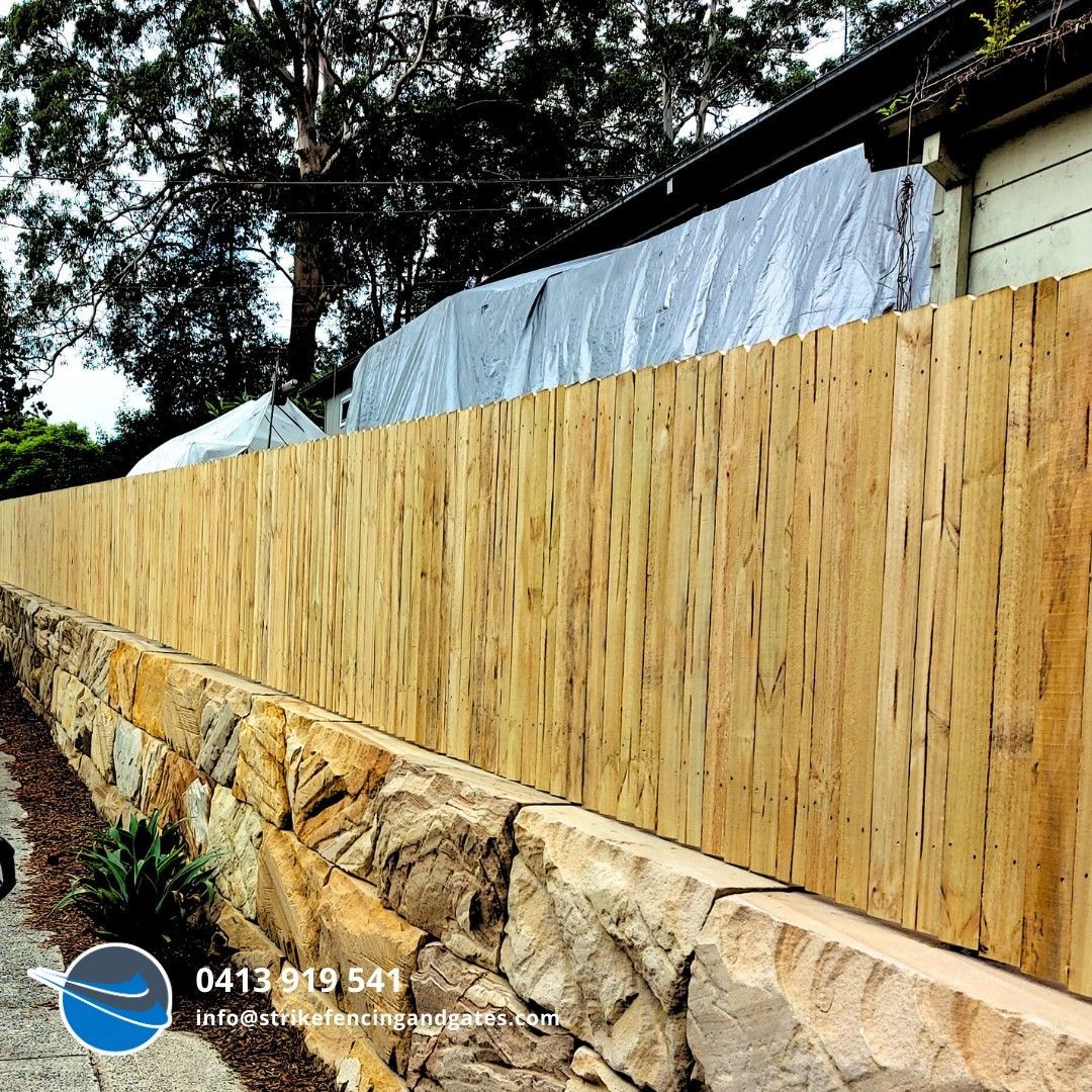 Wooden fence atop a stone wall, bordering a property, with trees in the background.