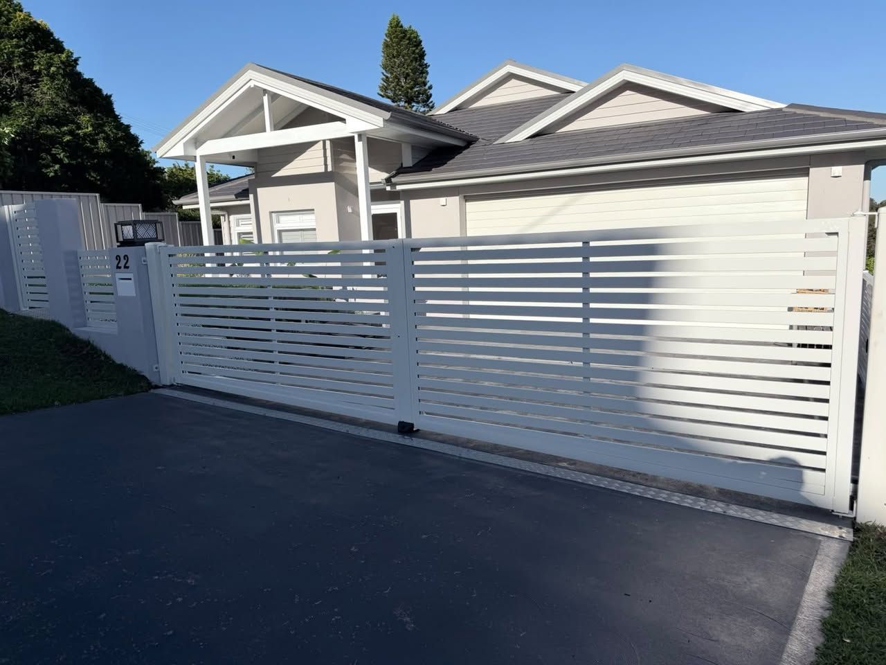 White slatted fence in front of a light-colored house with a driveway and carport — Strike Fencing & Gates In Woy Woy, NSW
