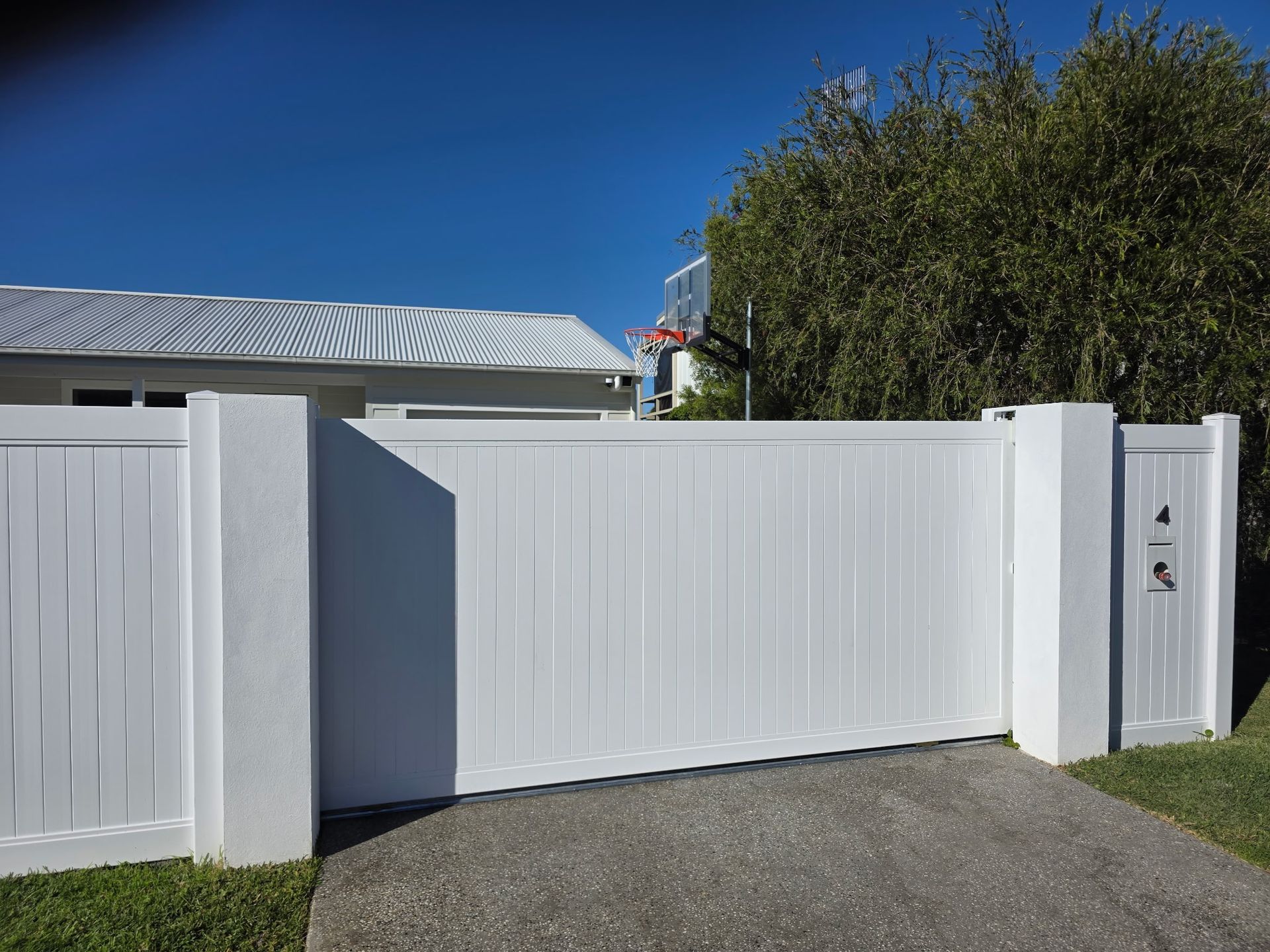 White driveway gate and fence with mailbox beside a suburban home under a clear blue sky — Strike Fencing & Gates In Terrigal, NSW