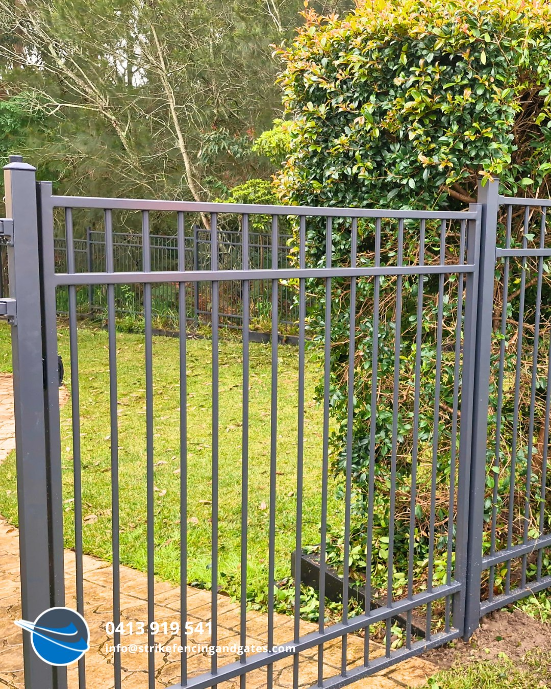 Dark Grey Metal Fence In Front Of A Green Lawn And Bush