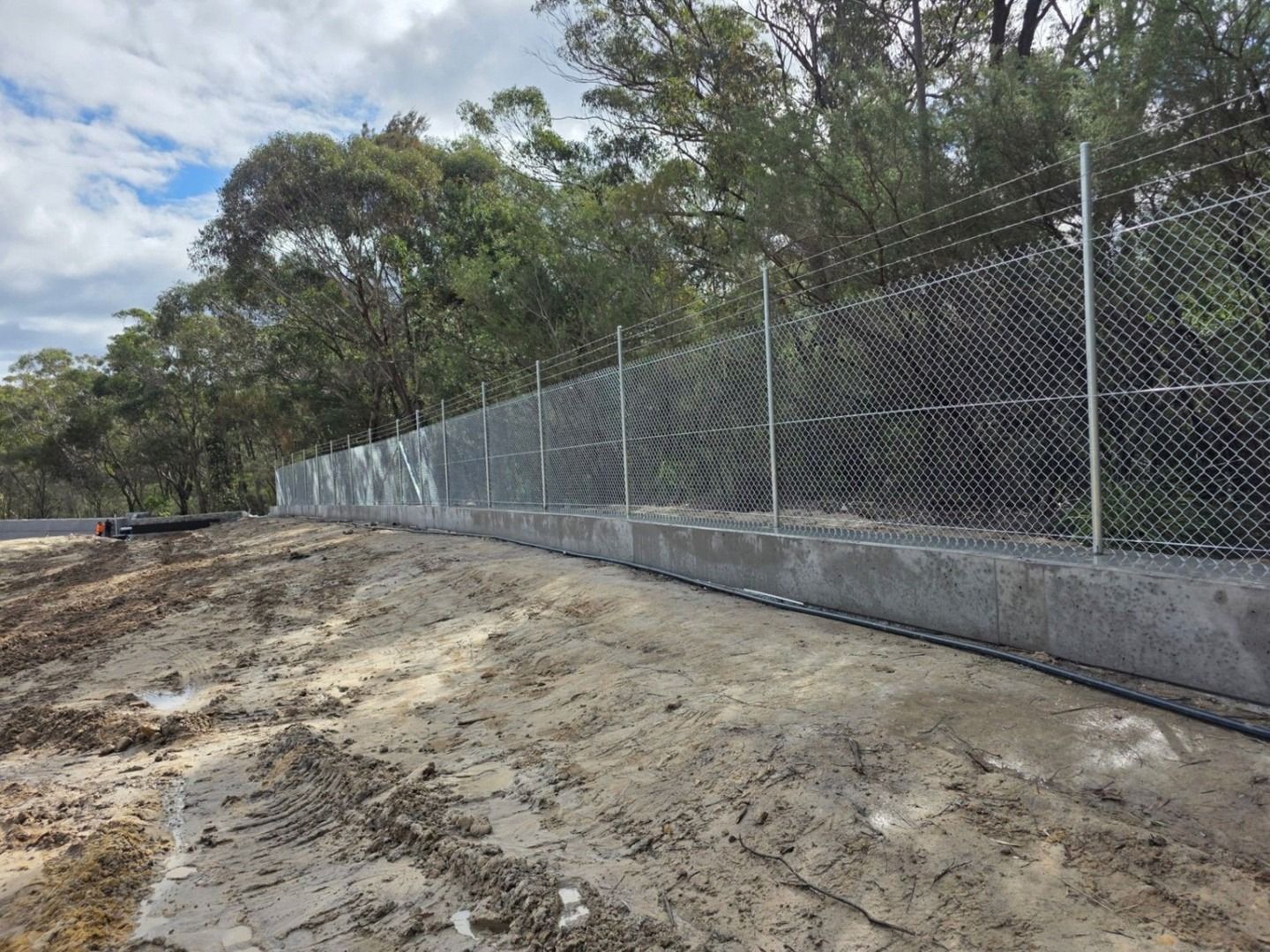 Chain-Link Fence Along a Dirt Roadside Beside Trees — Strike Fencing & Gates In Gosford, NSW