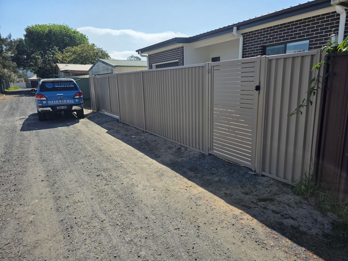 Blue Pickup Truck Parked on A Gravel Road Beside a Beige Fence — Strike Fencing & Gates In Tuggerah, NSW