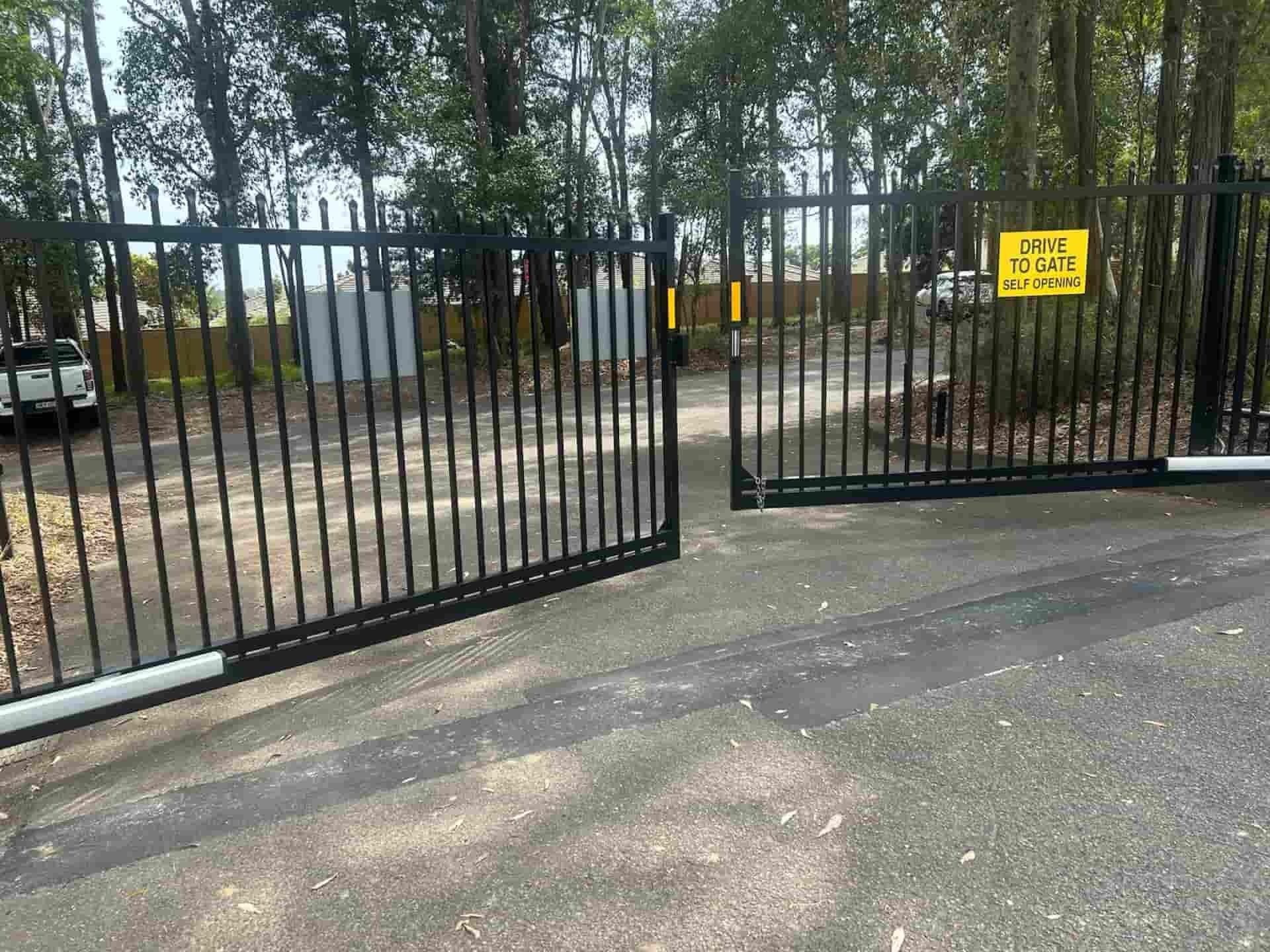 Black Metal Gates, Partially Open, Lead to a Dirt Road — Strike Fencing & Gates In Bateau Bay, NSW