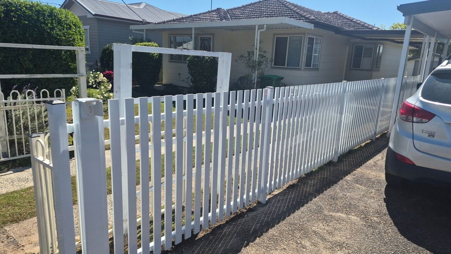 White Picket Fence Along a Suburban Driveway Beside a Parked Silver Car — Strike Fencing & Gates In Umina, NSW
