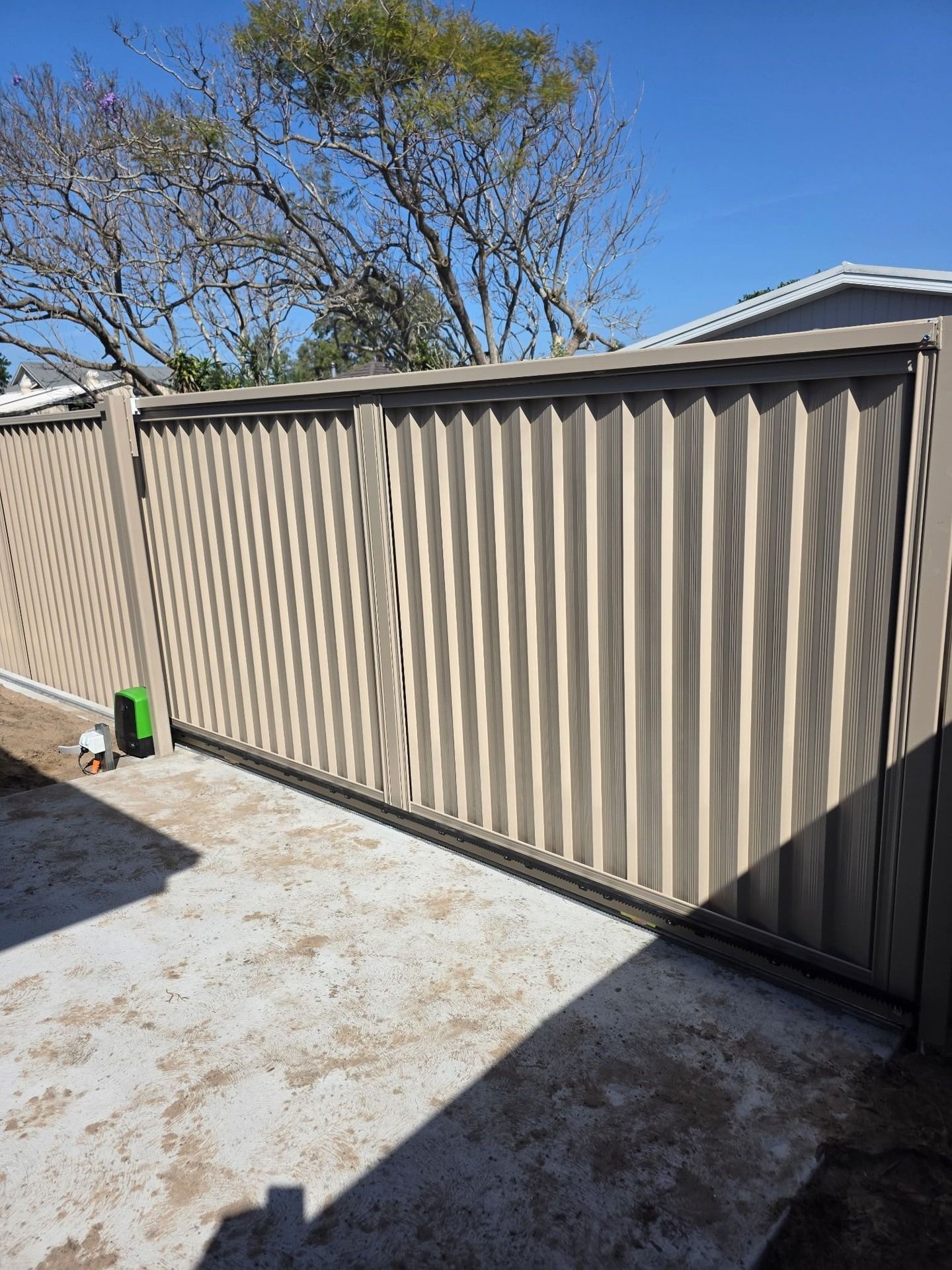 Beige Corrugated Metal Fence Along a Concrete Driveway — Strike Fencing & Gates In Tuggerah, NSW