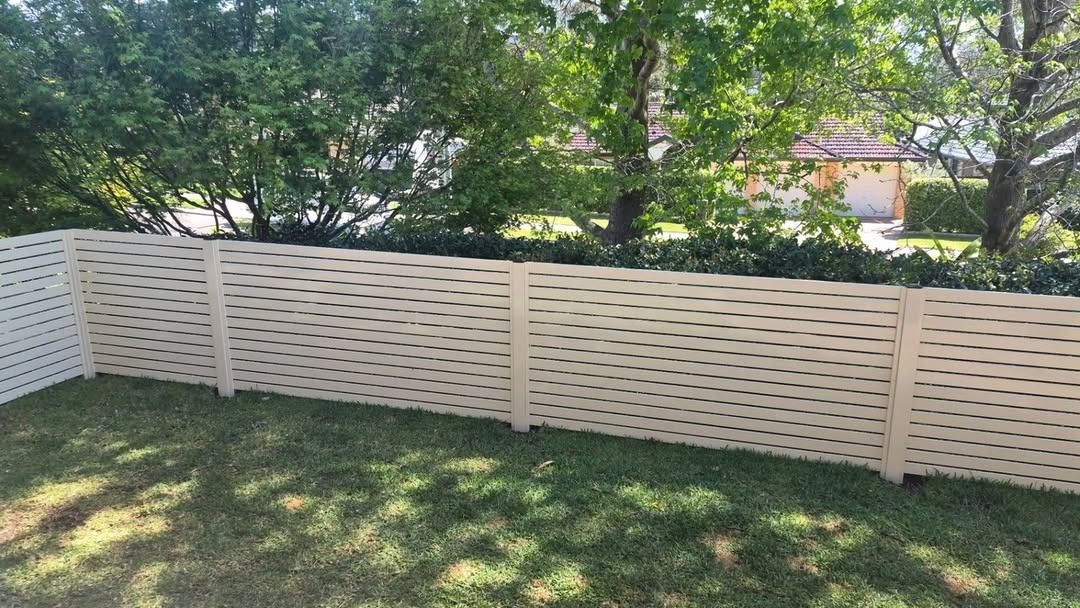 White Lattice Fence Around a Grassy Yard with Trees and A House — Strike Fencing & Gates In Terrigal, NSW